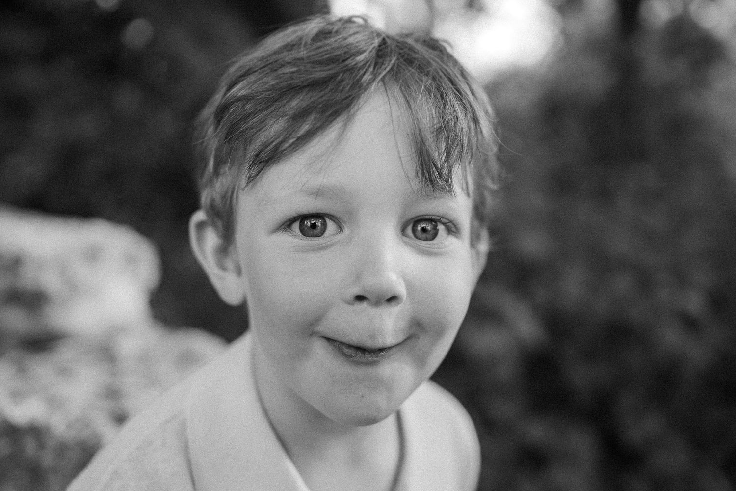 A close-up black and white portrait capturing a joyful expression outdoors.