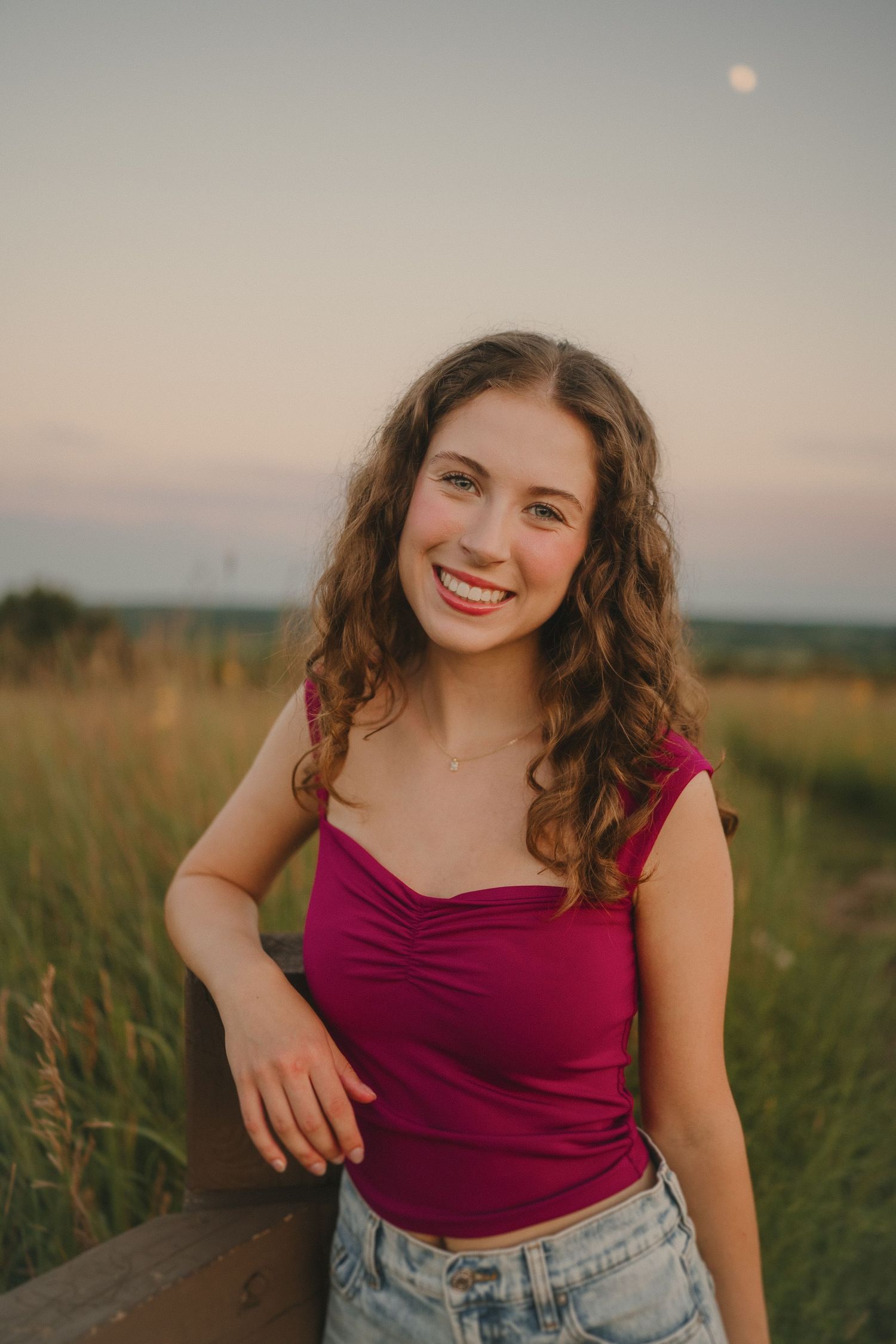 Portrait in a field at sunset with golden light, wearing a burgundy top and denim shorts.