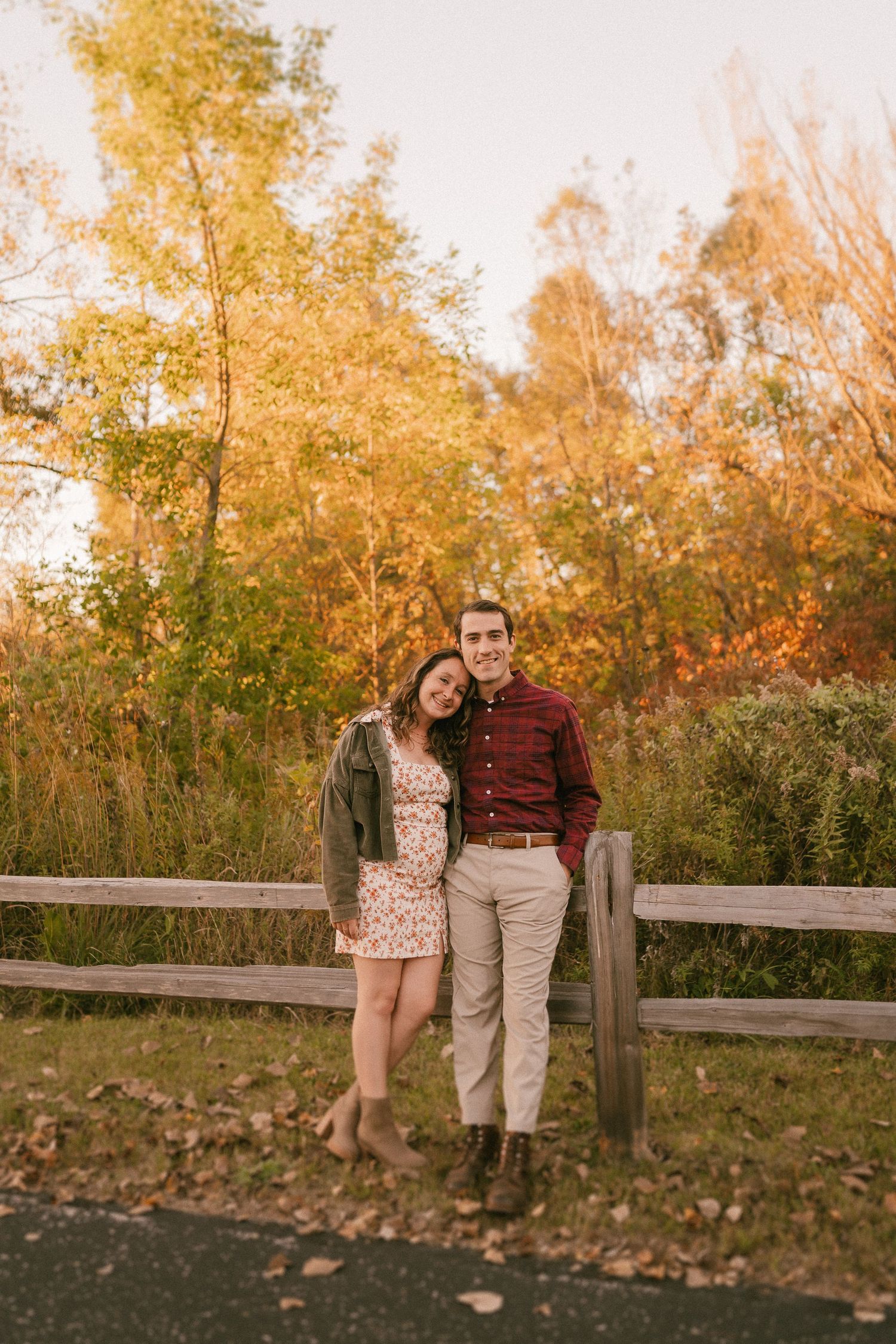 Couple poses by wooden fence during golden autumn afternoon.