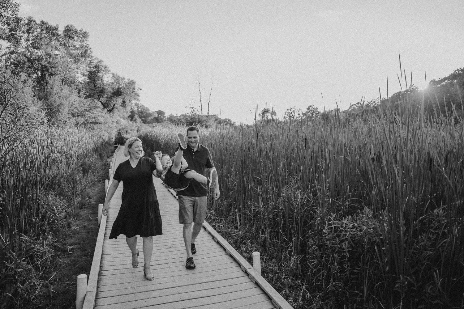 Family walking together on elevated wooden pathway through marsh landscape.