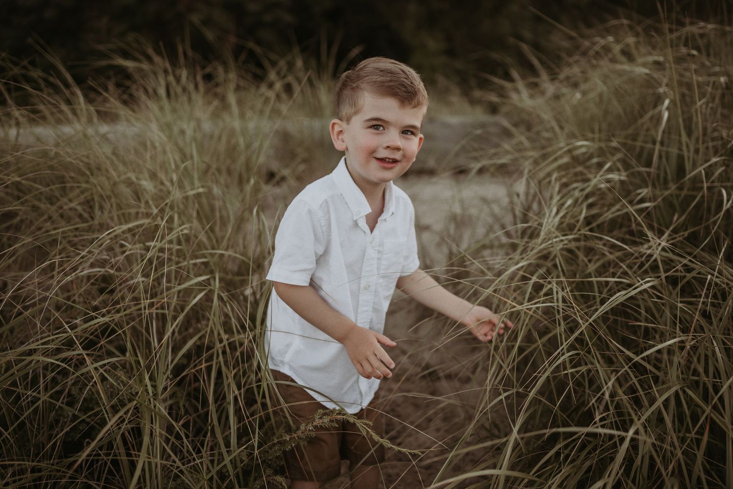 A playful child running through tall beach grass in warm evening light.