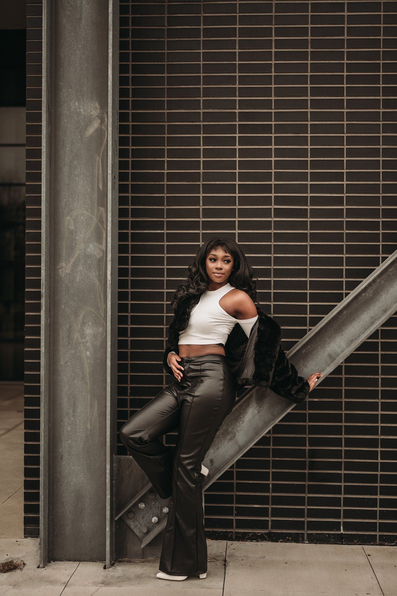 Model in retro outfit poses against textured brick wall with industrial elements.