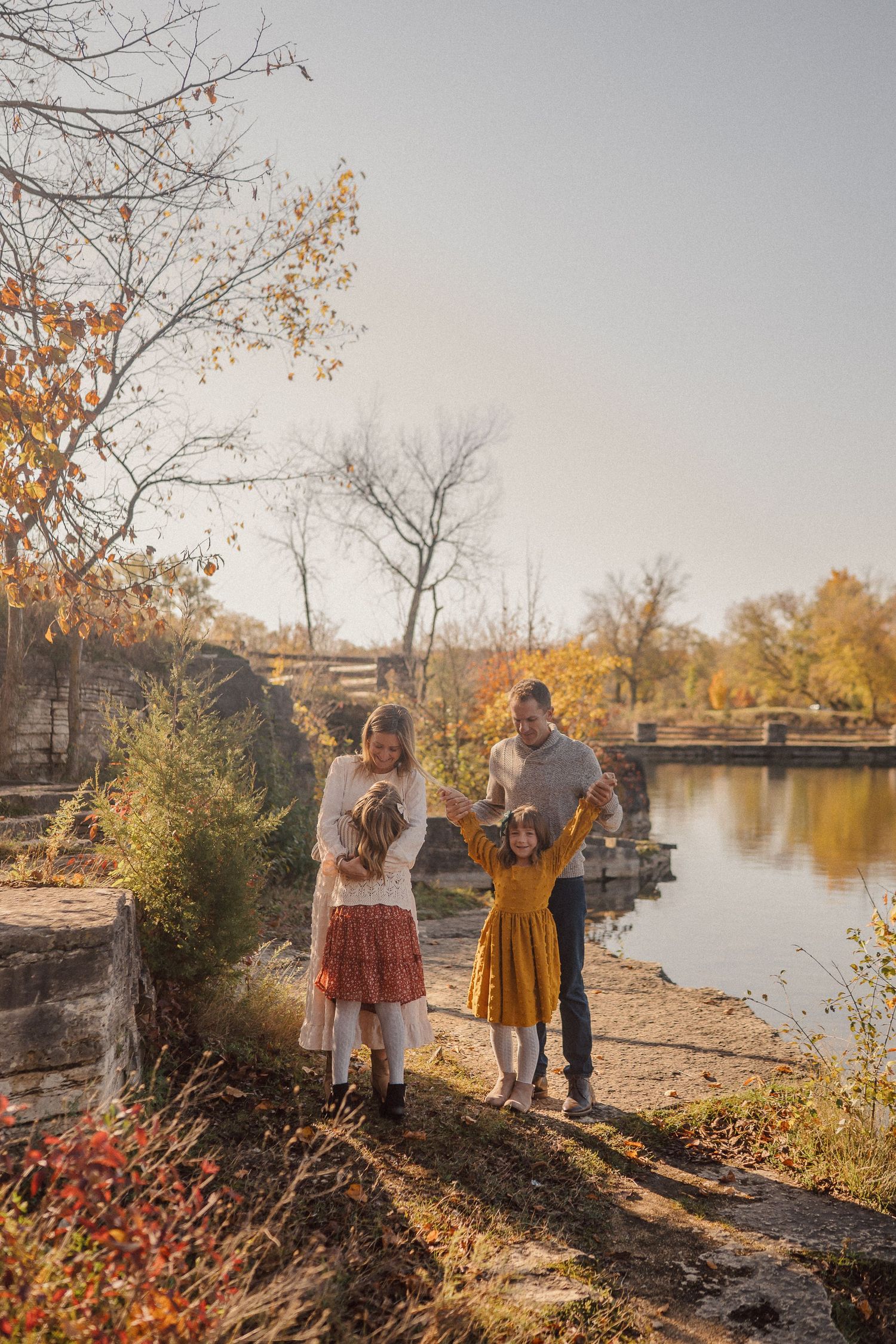 A family enjoying an autumn day by a lake with fall foliage and stone bridge in background.