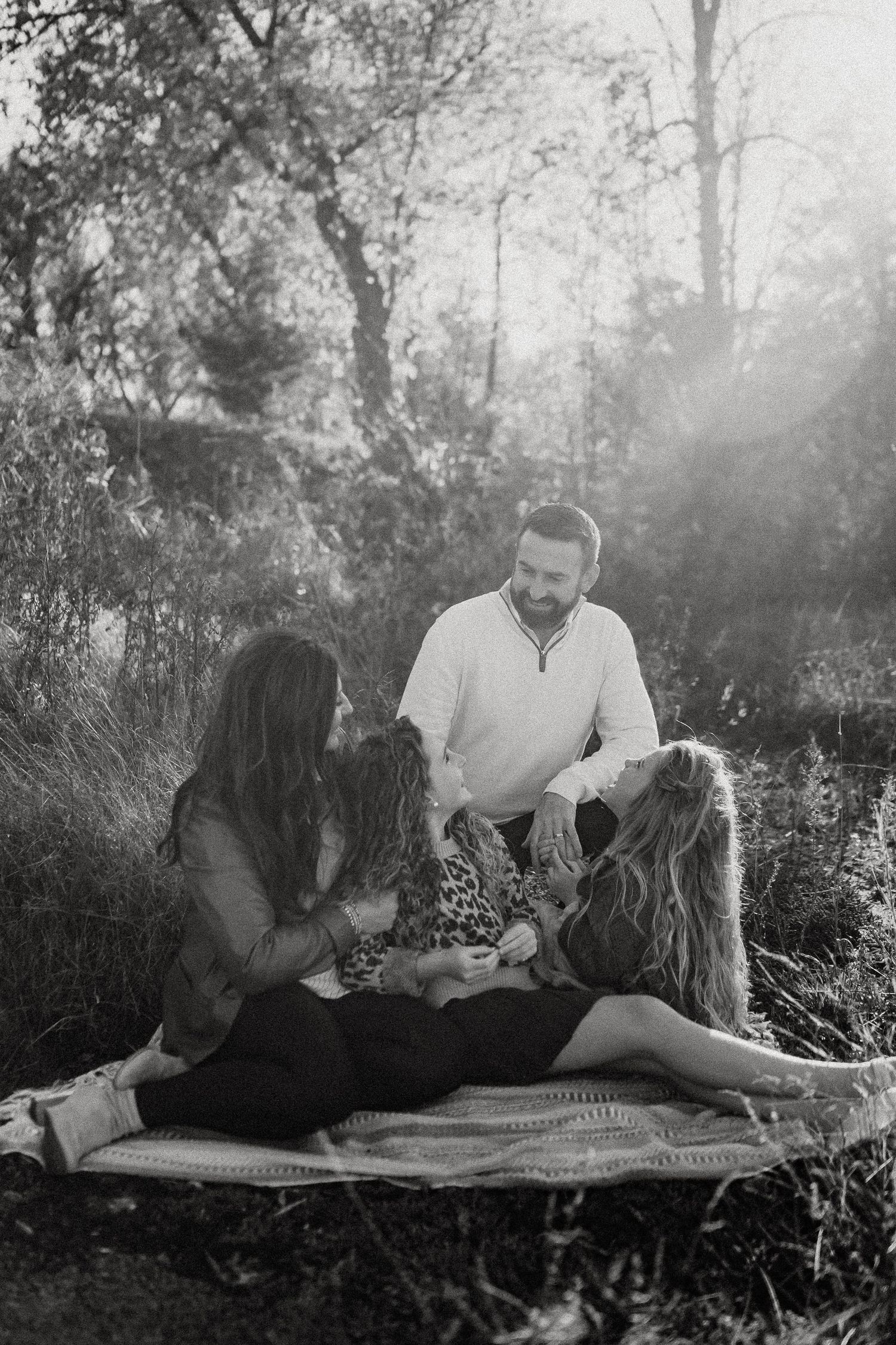 A family enjoys a picnic together on a blanket in a sunlit forest setting.