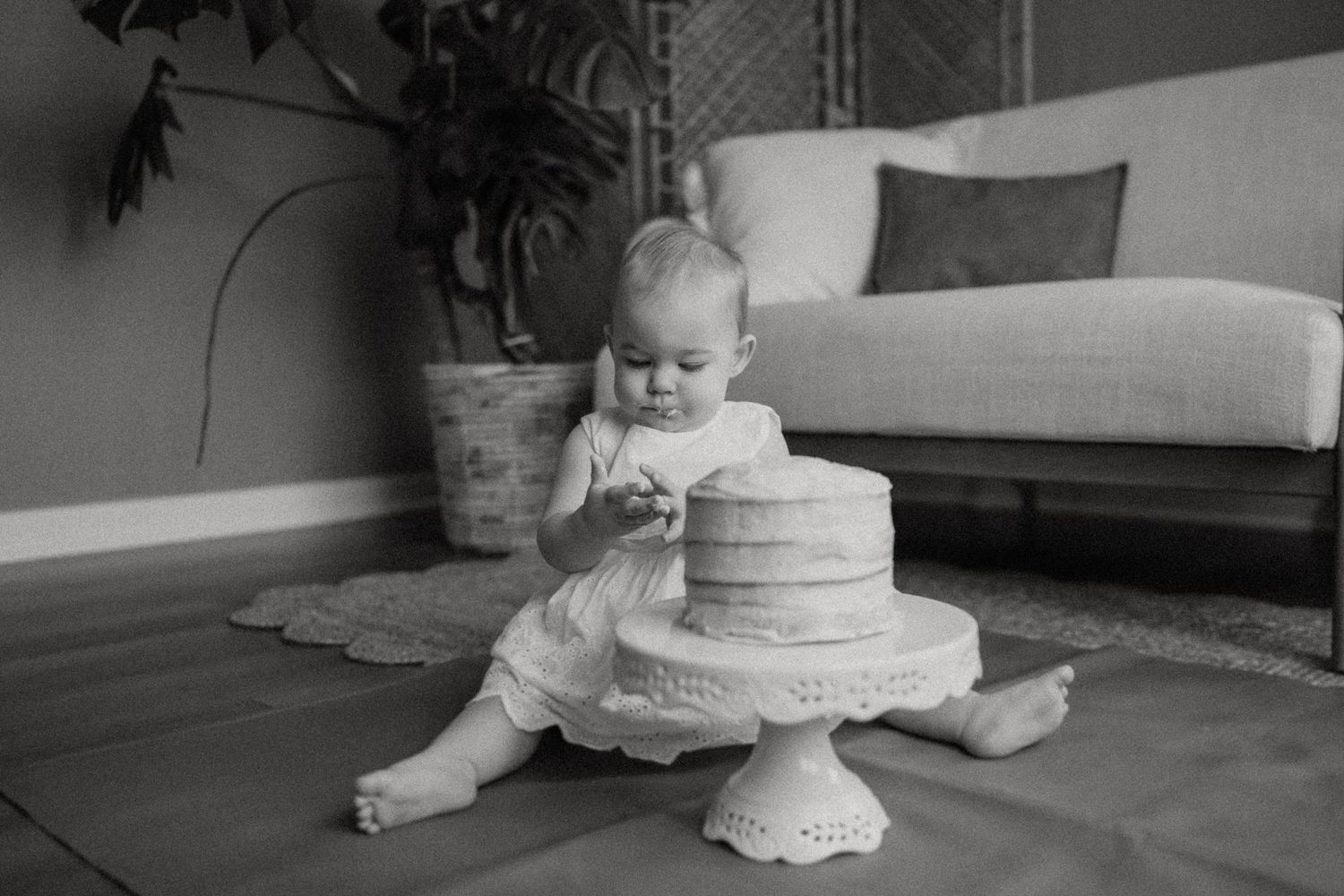 Black and white photo of a cake smash session with a simple two-tier cake on an ornate pedestal.