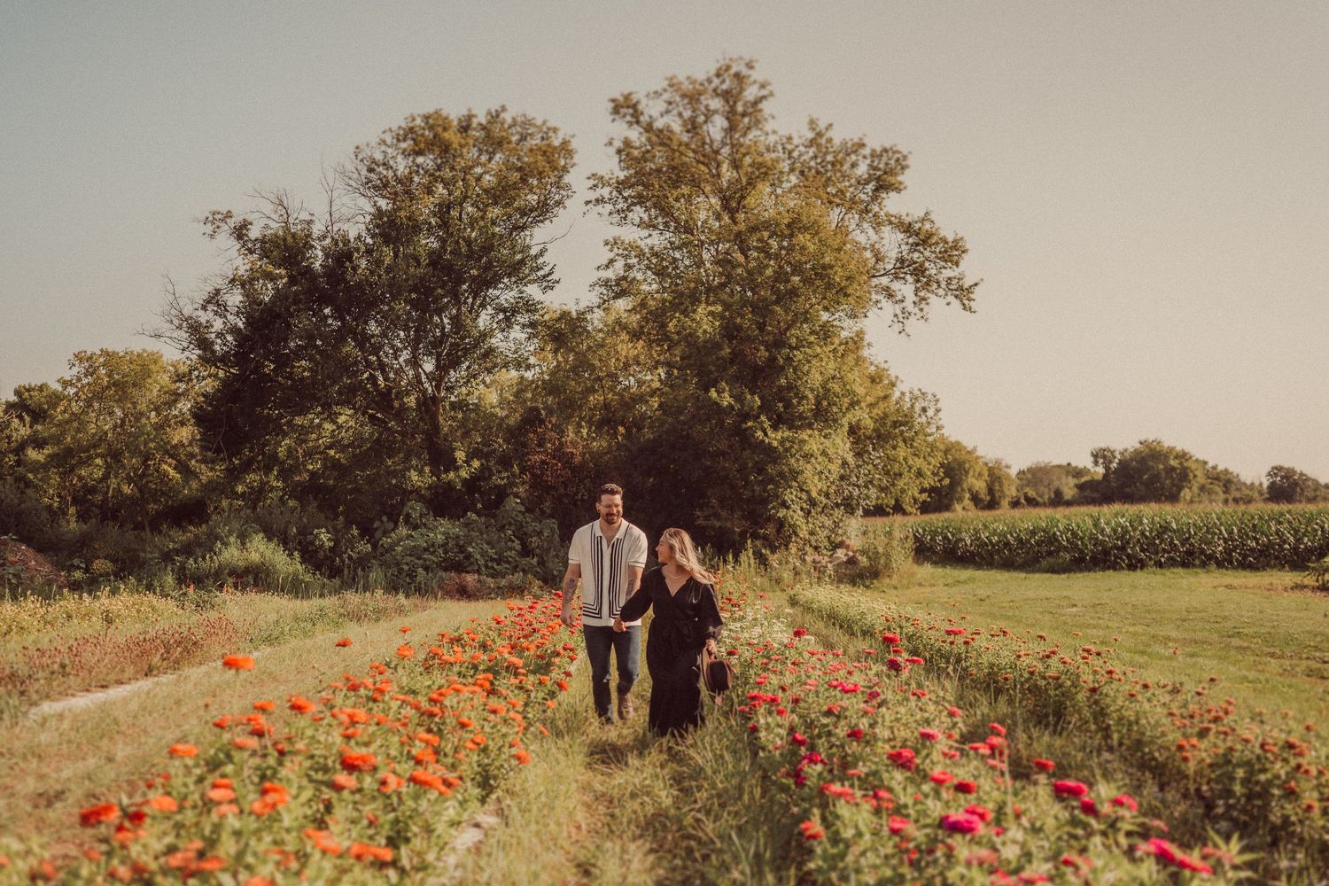 A couple walks hand in hand through a beautiful garden path lined with red poppies.