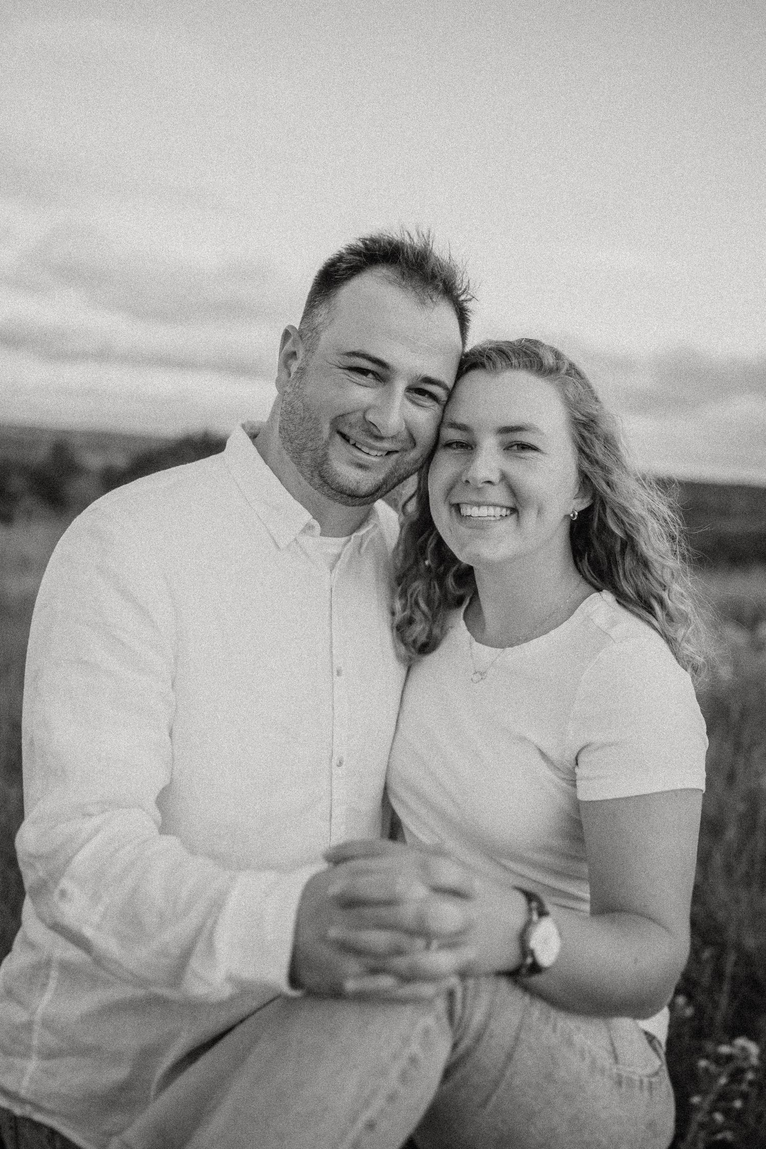 Black and white portrait of couple embracing in outdoor field setting.