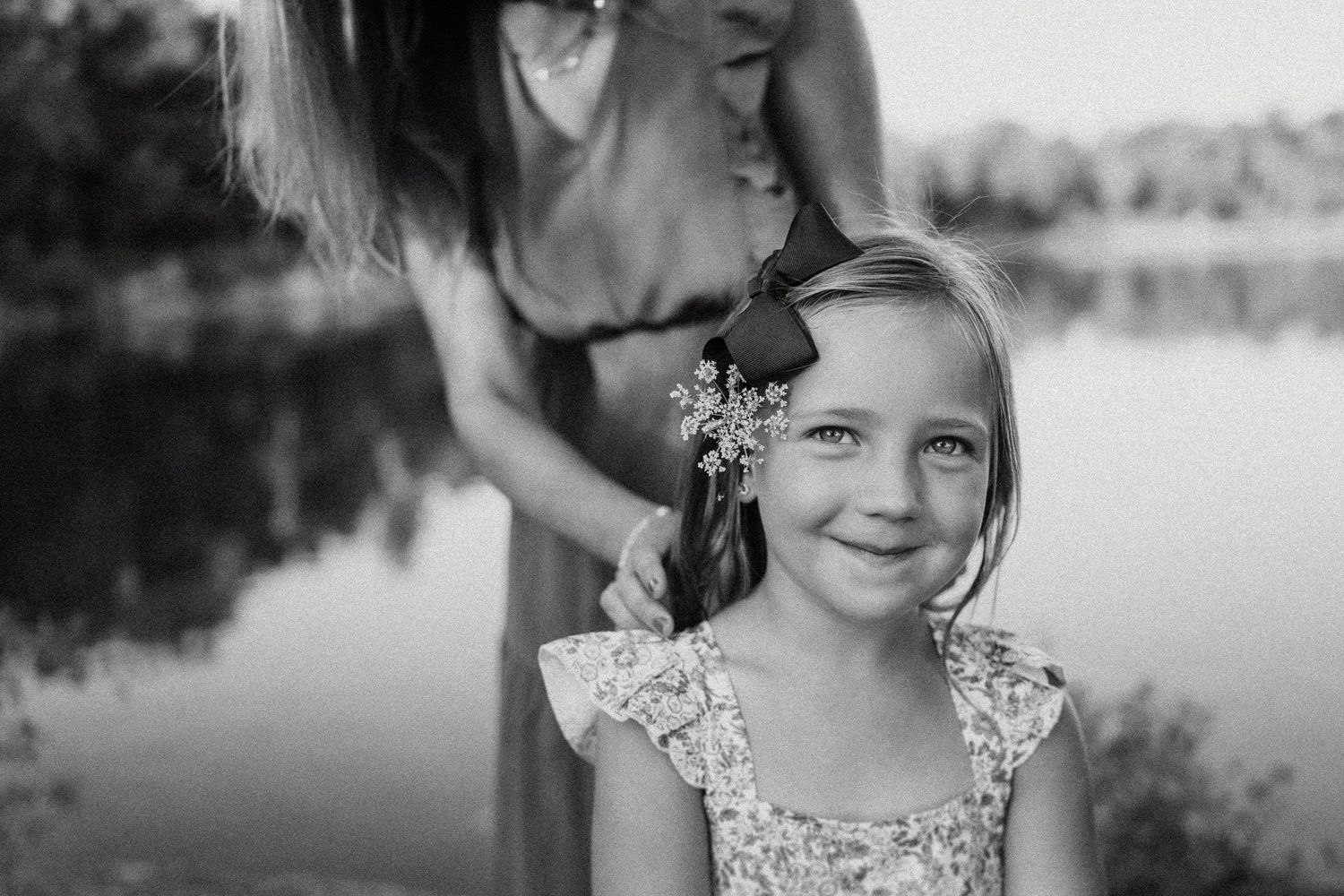 Black and white portrait by a lake with delicate flowers and soft lighting.