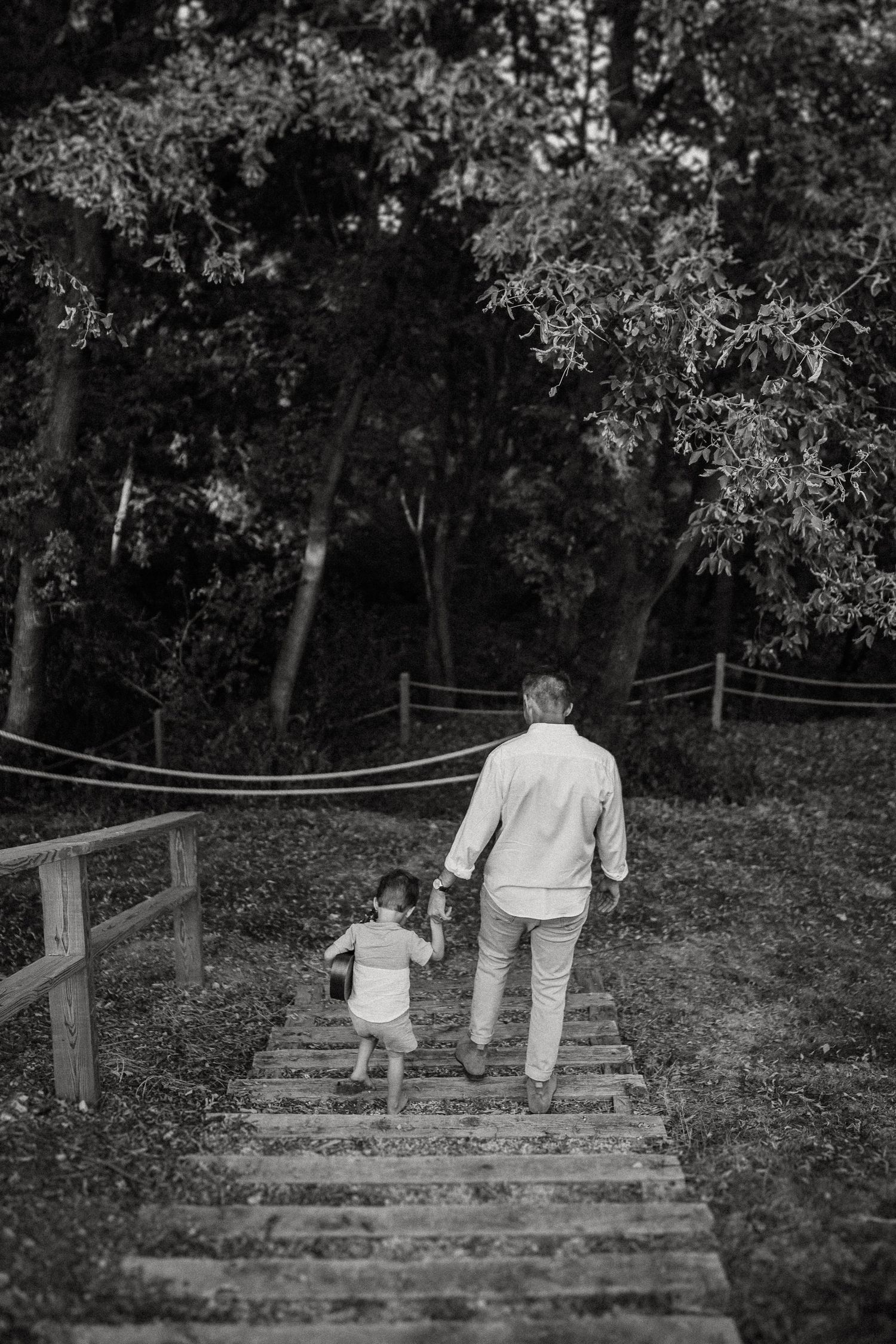 Parent and child walking down wooden steps together in a wooded area.