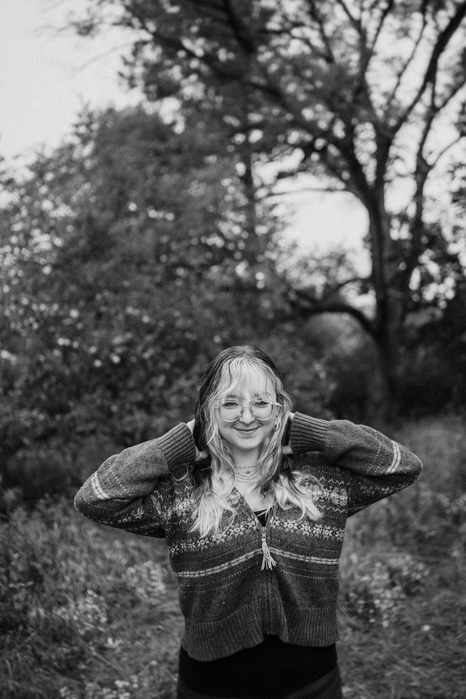 Black and white portrait showing someone in a patterned sweater expressing joy outdoors.
