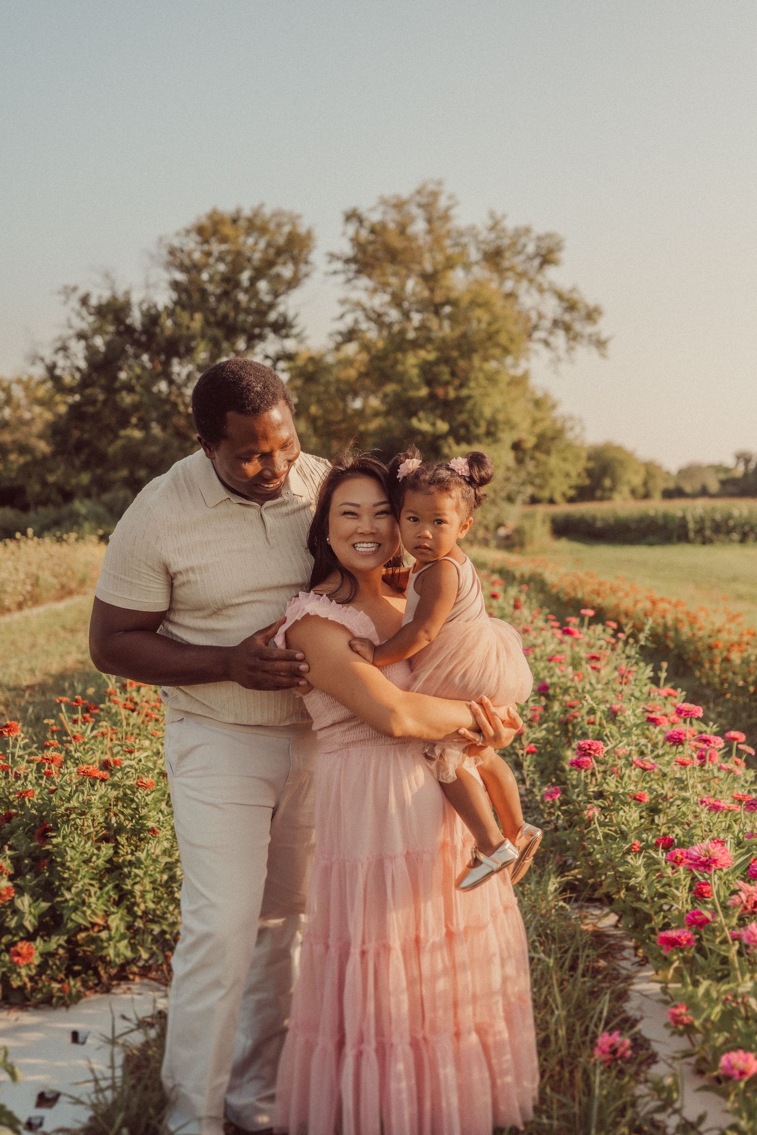 A loving family embrace in a garden path filled with pink flowers at sunset.