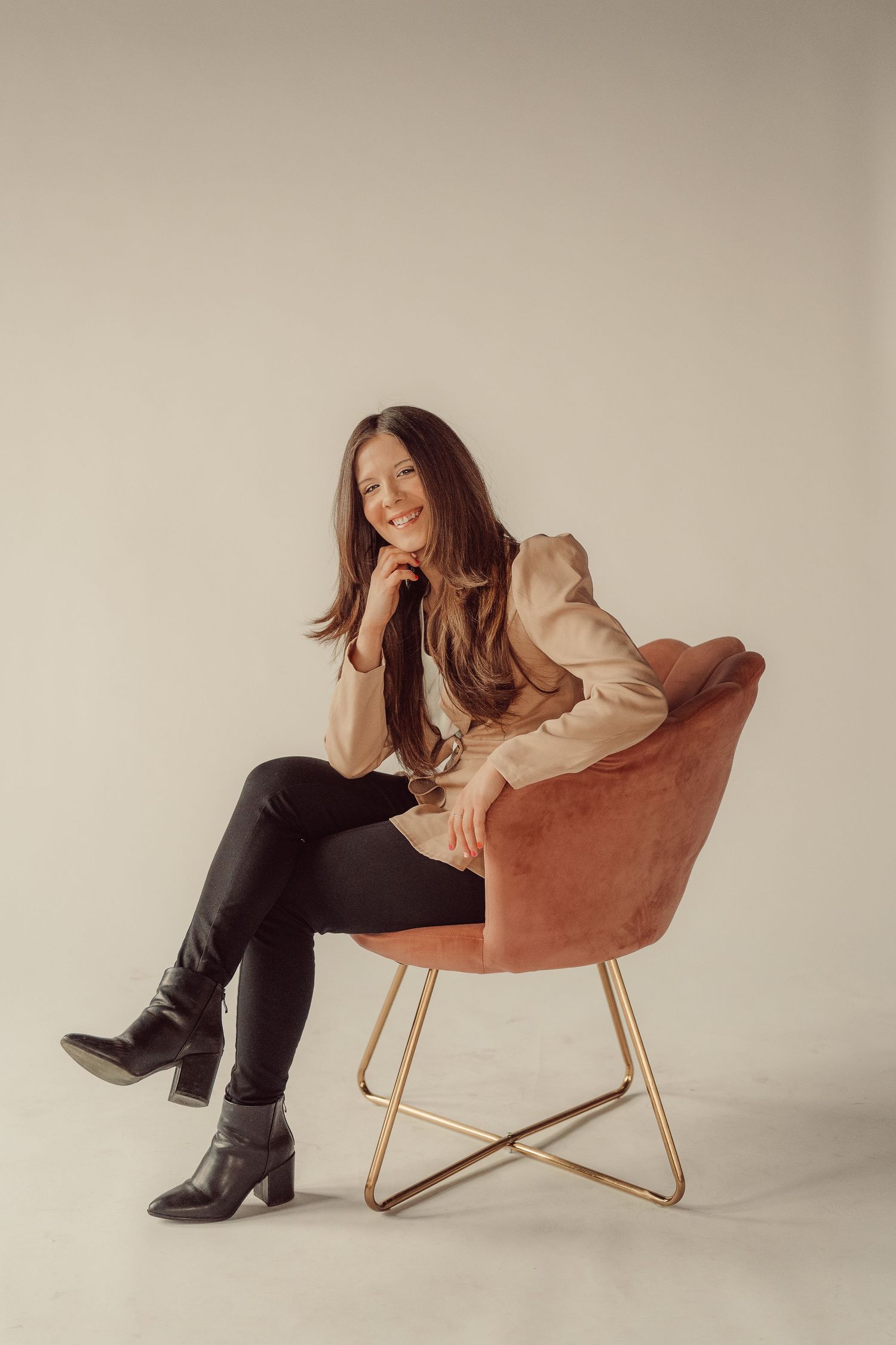 Woman in beige blazer relaxing in velvet orange chair during studio photoshoot.