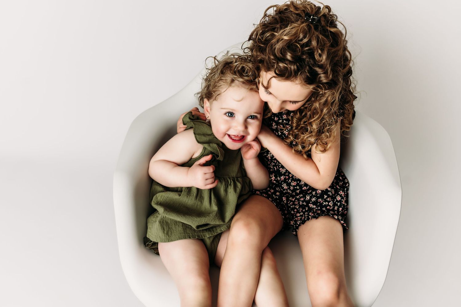 Two children sharing a sweet moment while sitting together in a white chair.