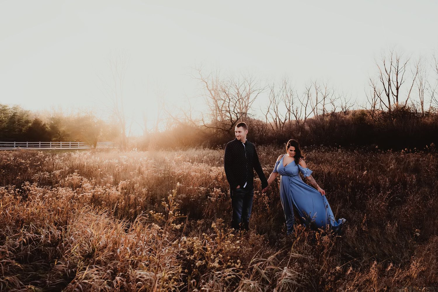 Couple posing in tall grass during golden hour with dramatic lighting.