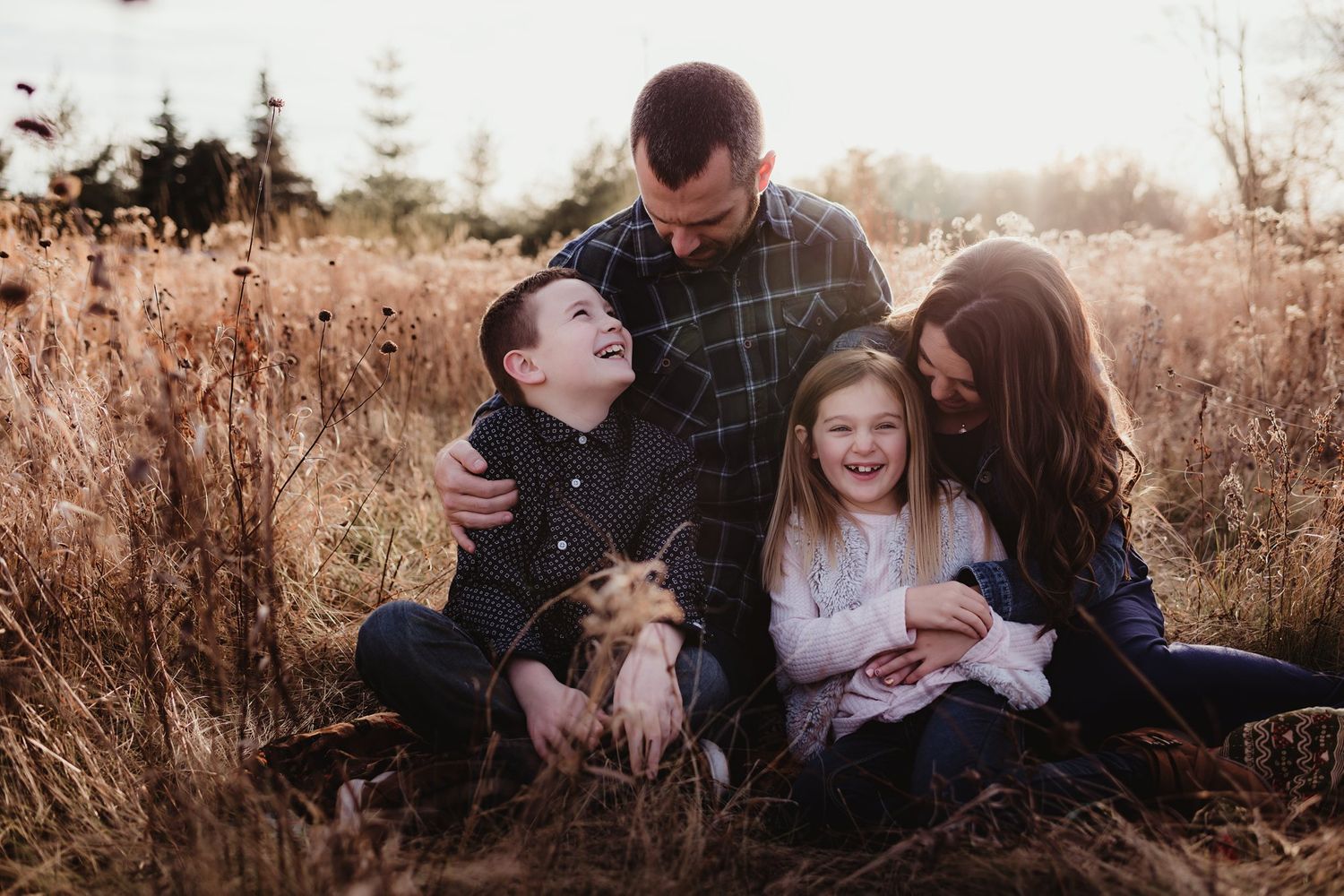 Family sitting together in tall golden grass during sunset photo session.