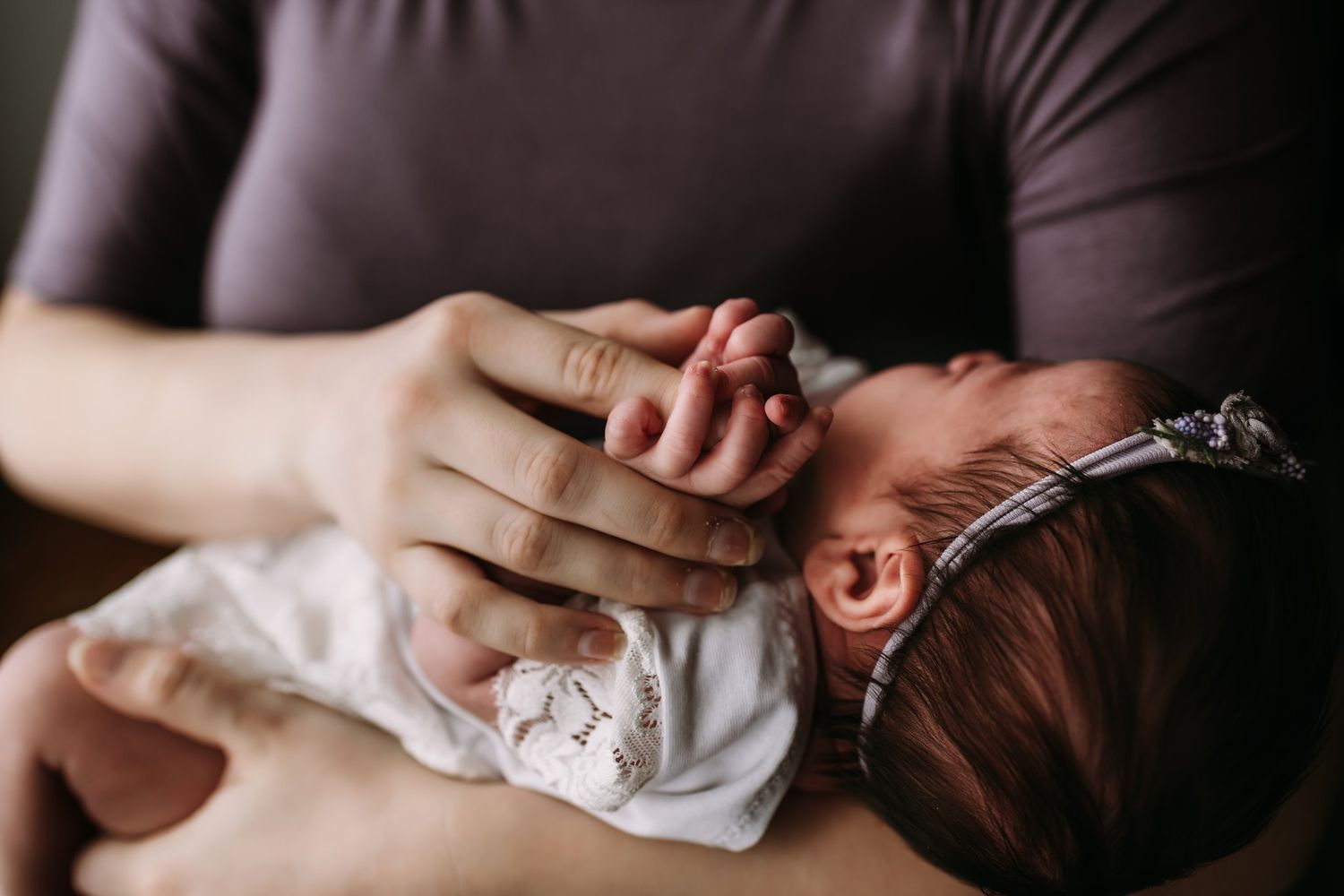 A tender moment captured of a newborn baby in white lace being cradled close.