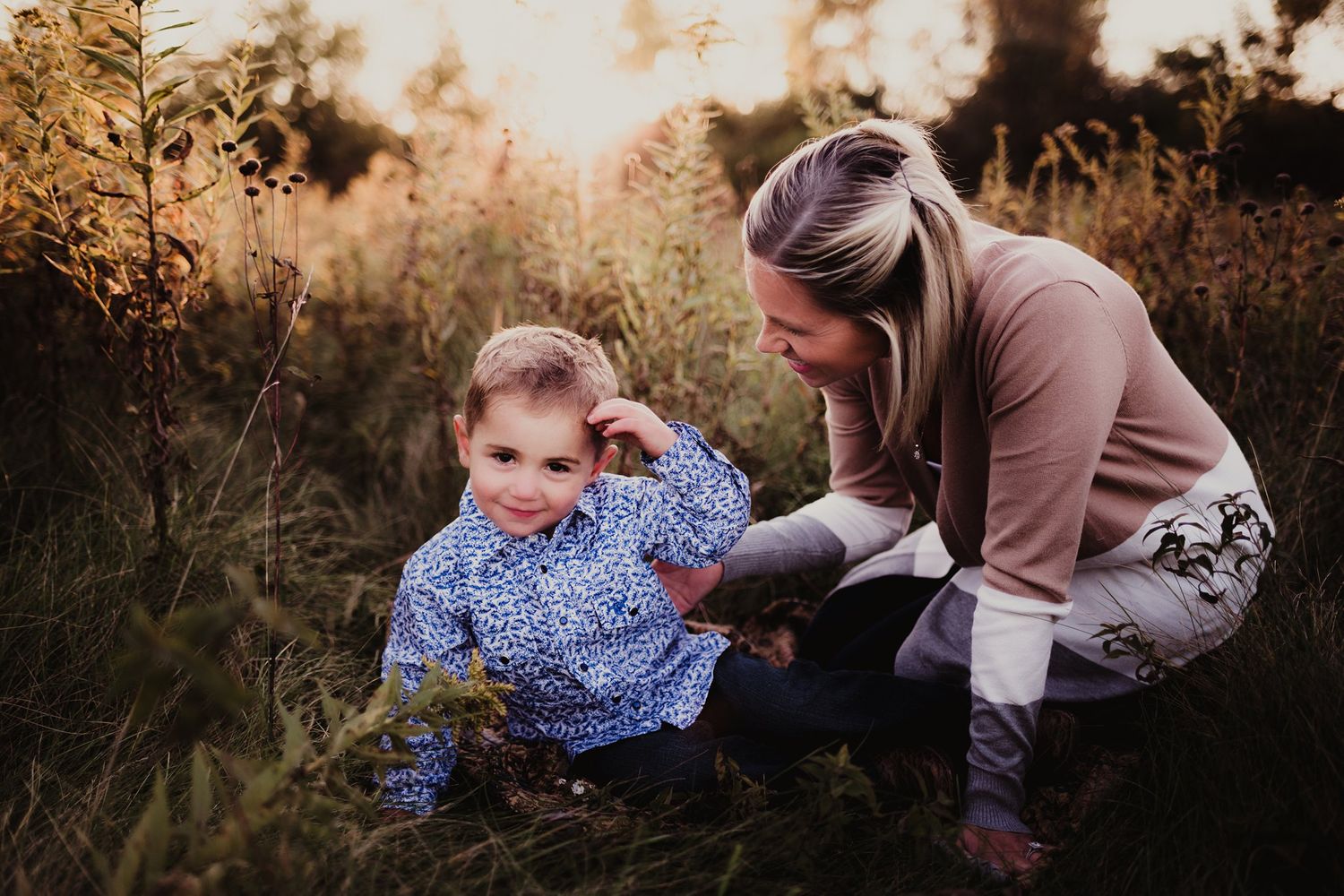 Candid outdoor photo of parent and young child playing in golden hour light among tall grasses.