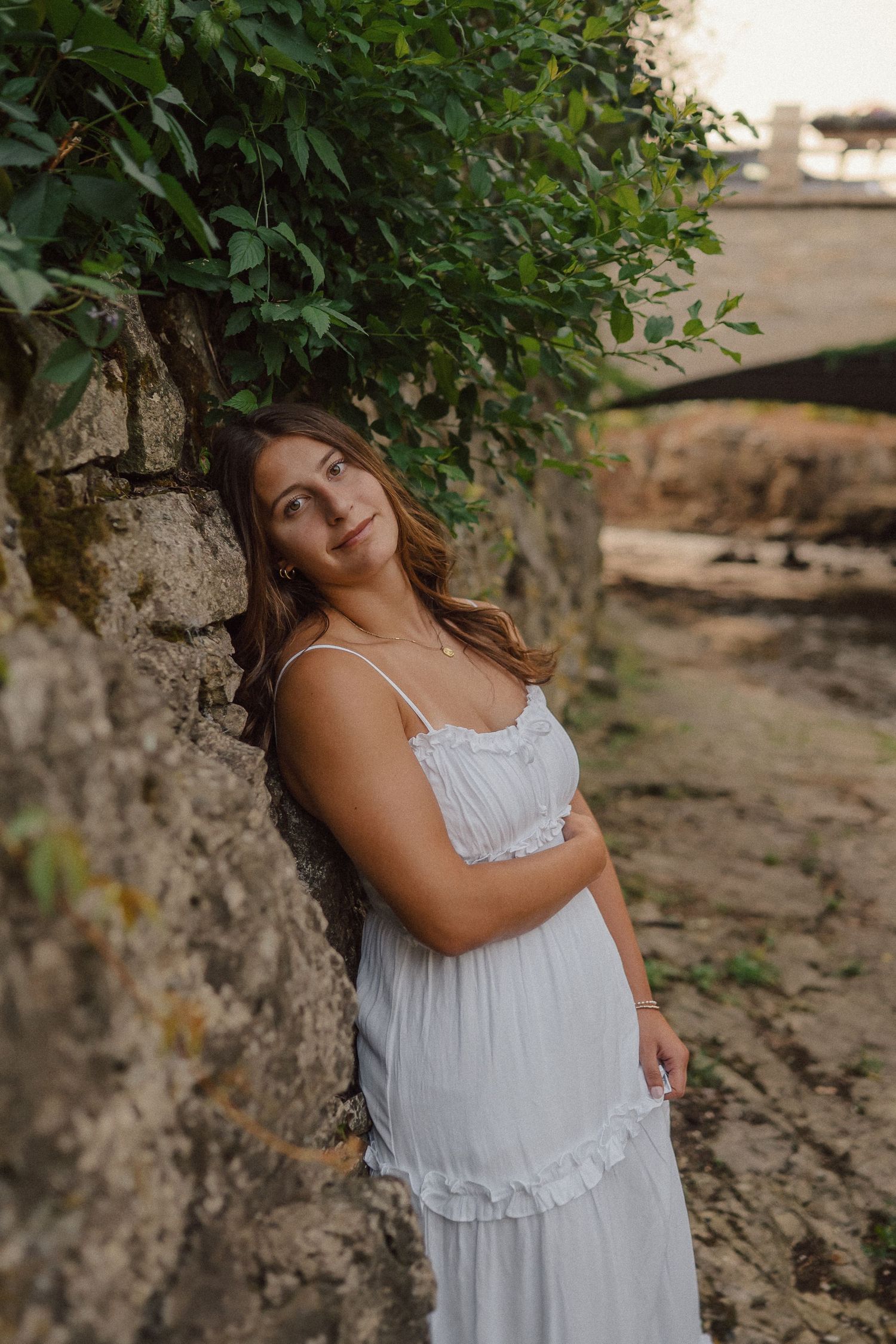 A white lace summer dress photographed against textured stone walls and green foliage.