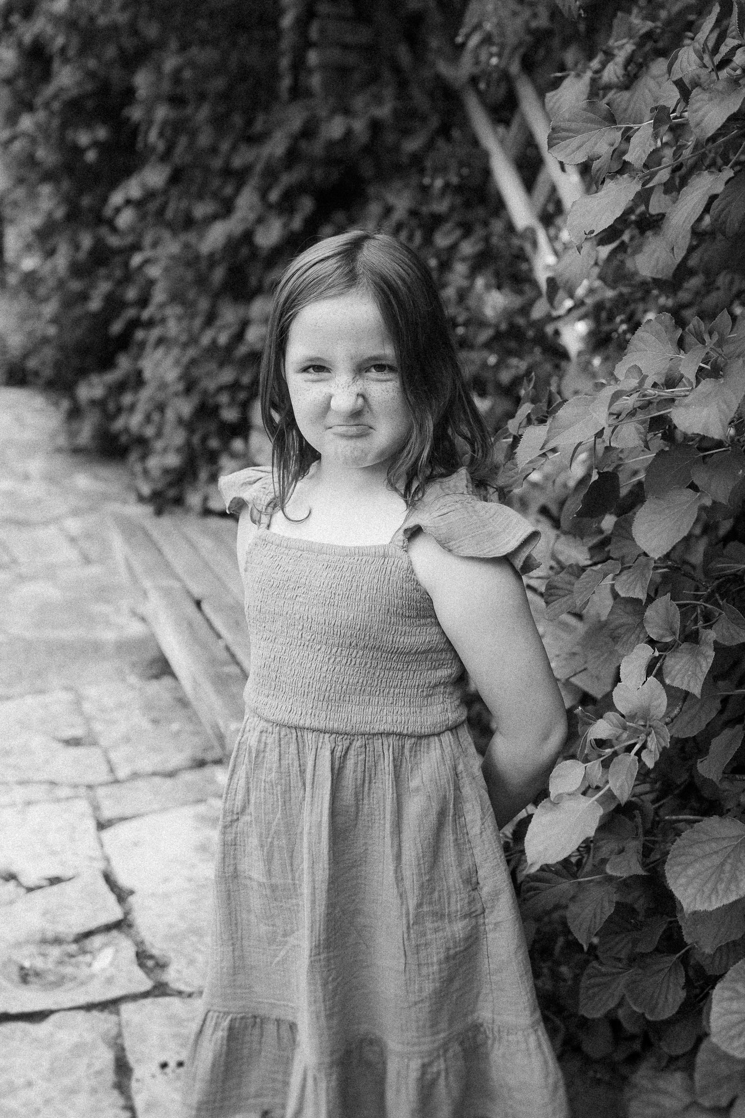 Black and white portrait in a garden setting with stone path and climbing vines.