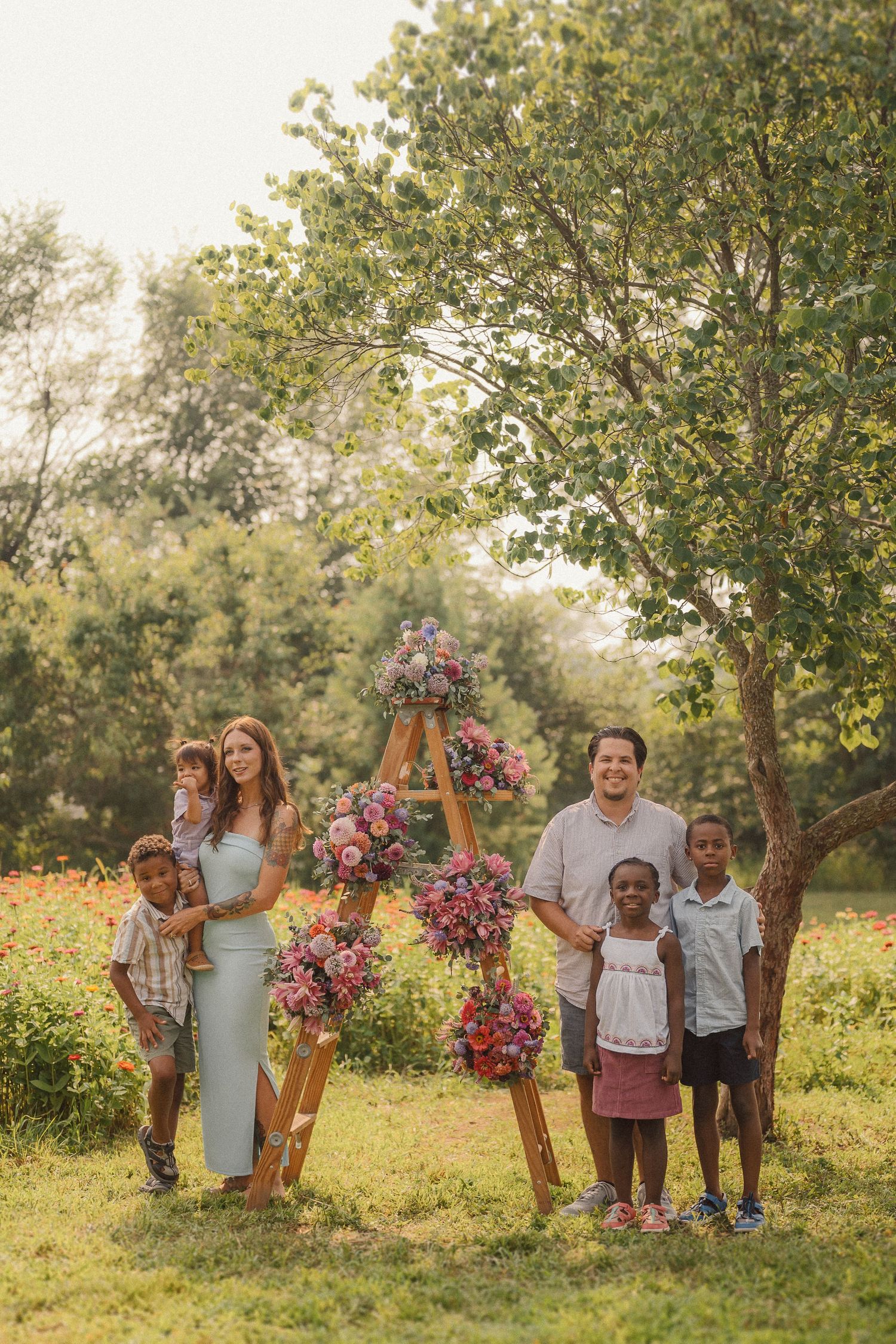 Group portrait of families gathered around wooden ladder with pink and purple flower arrangements.