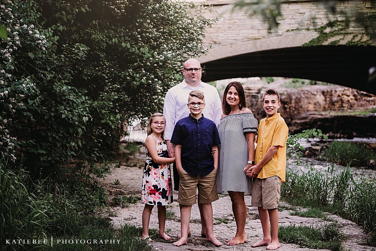 Small family group poses together under stone bridge in outdoor setting.