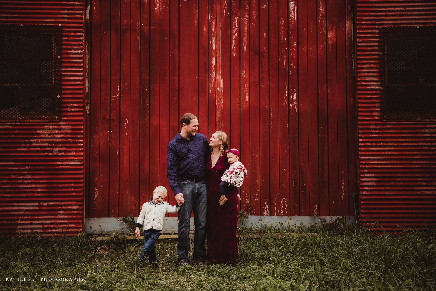 Family portrait against rustic red barn showcasing authentic connection and warmth.