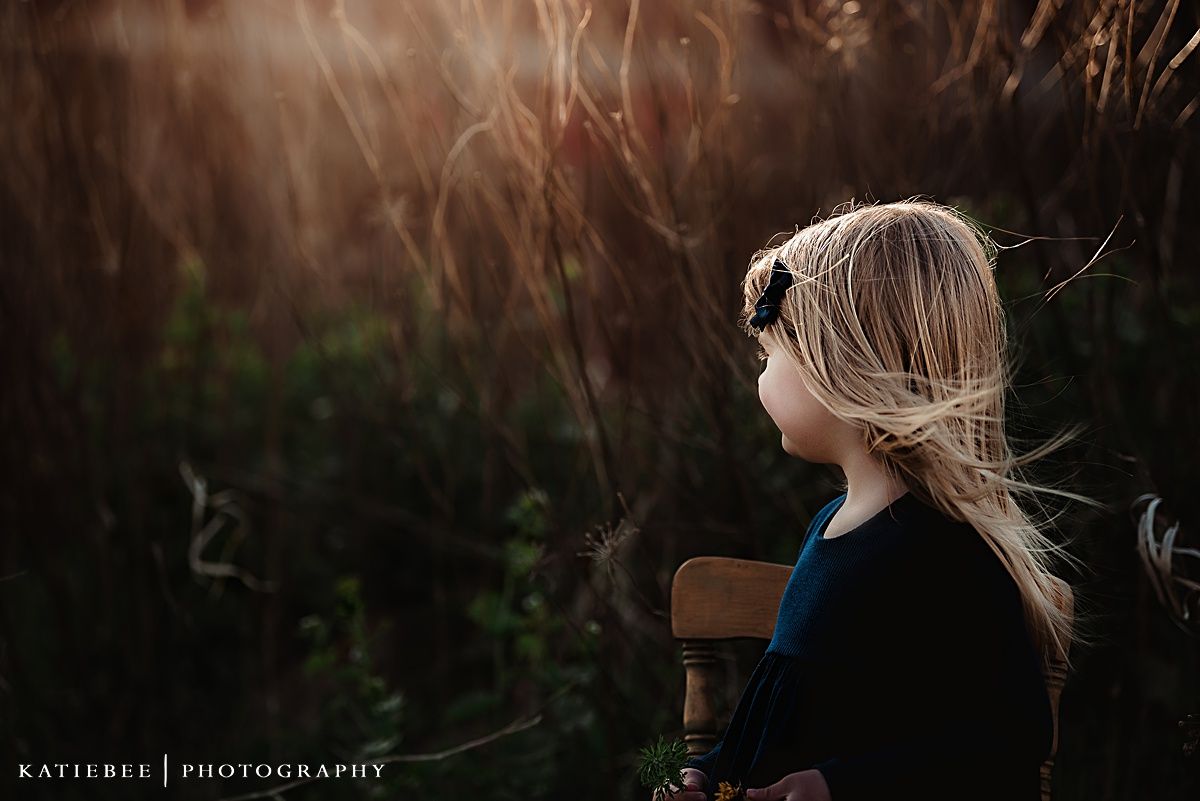 Side profile portrait of child looking up through tall grass at sunset.