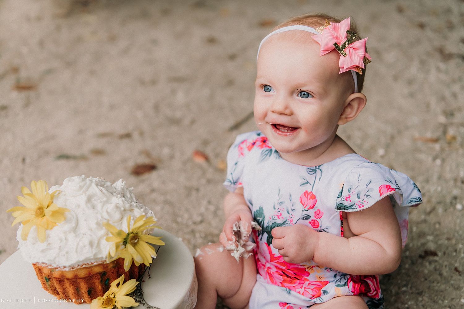 A small child in a floral dress sits by a decorated cupcake with flowers.