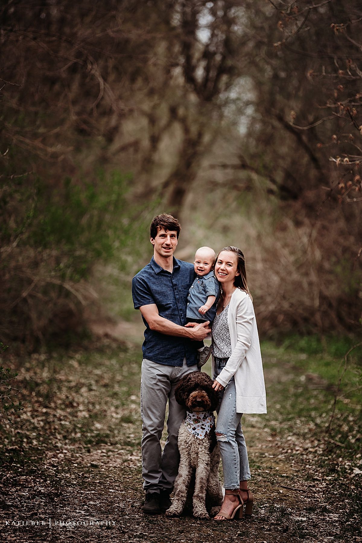 Family and dog pose together on wooded trail during outdoor photo session.