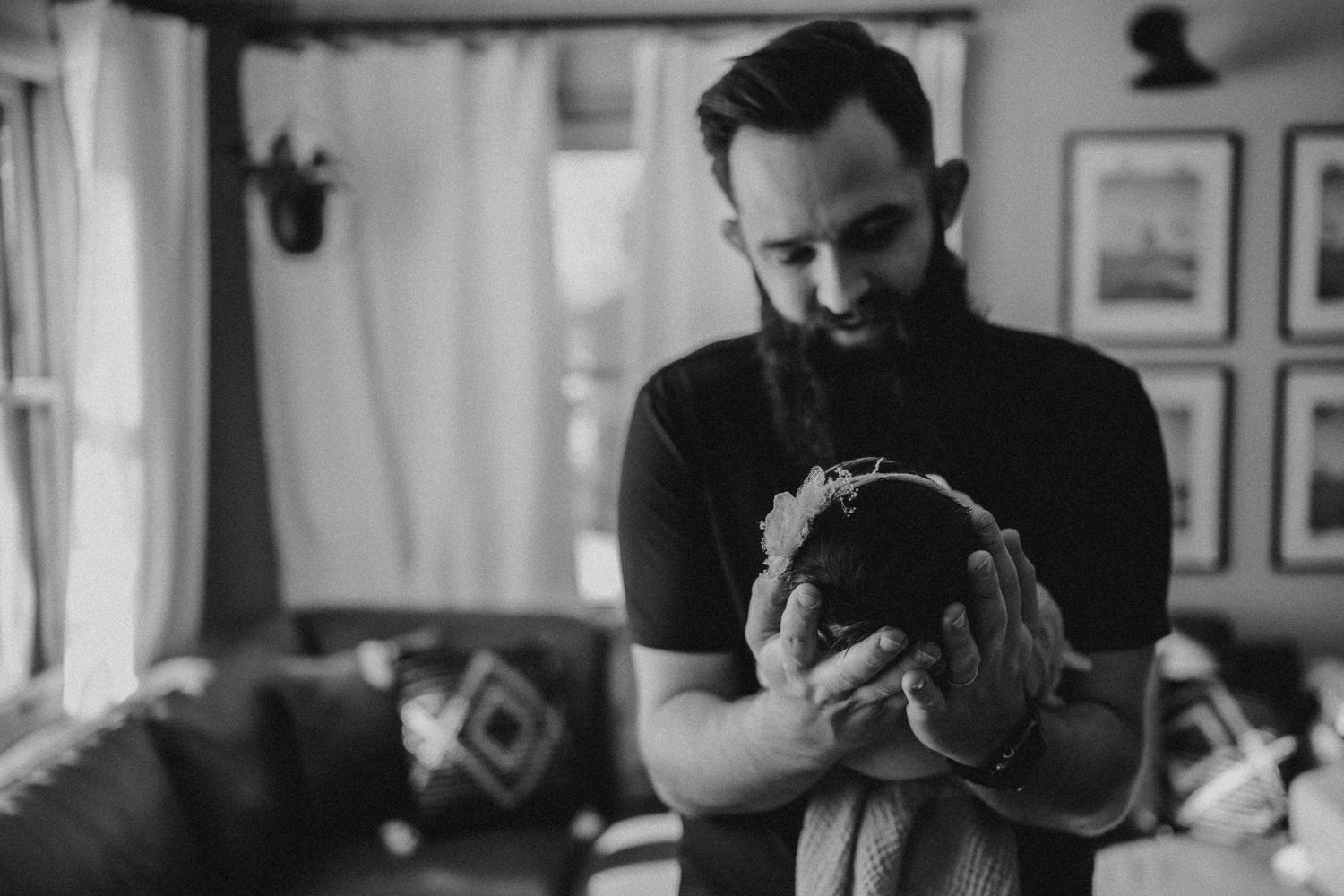 Person in black t-shirt tenderly holding sleeping newborn in a cozy indoor setting.