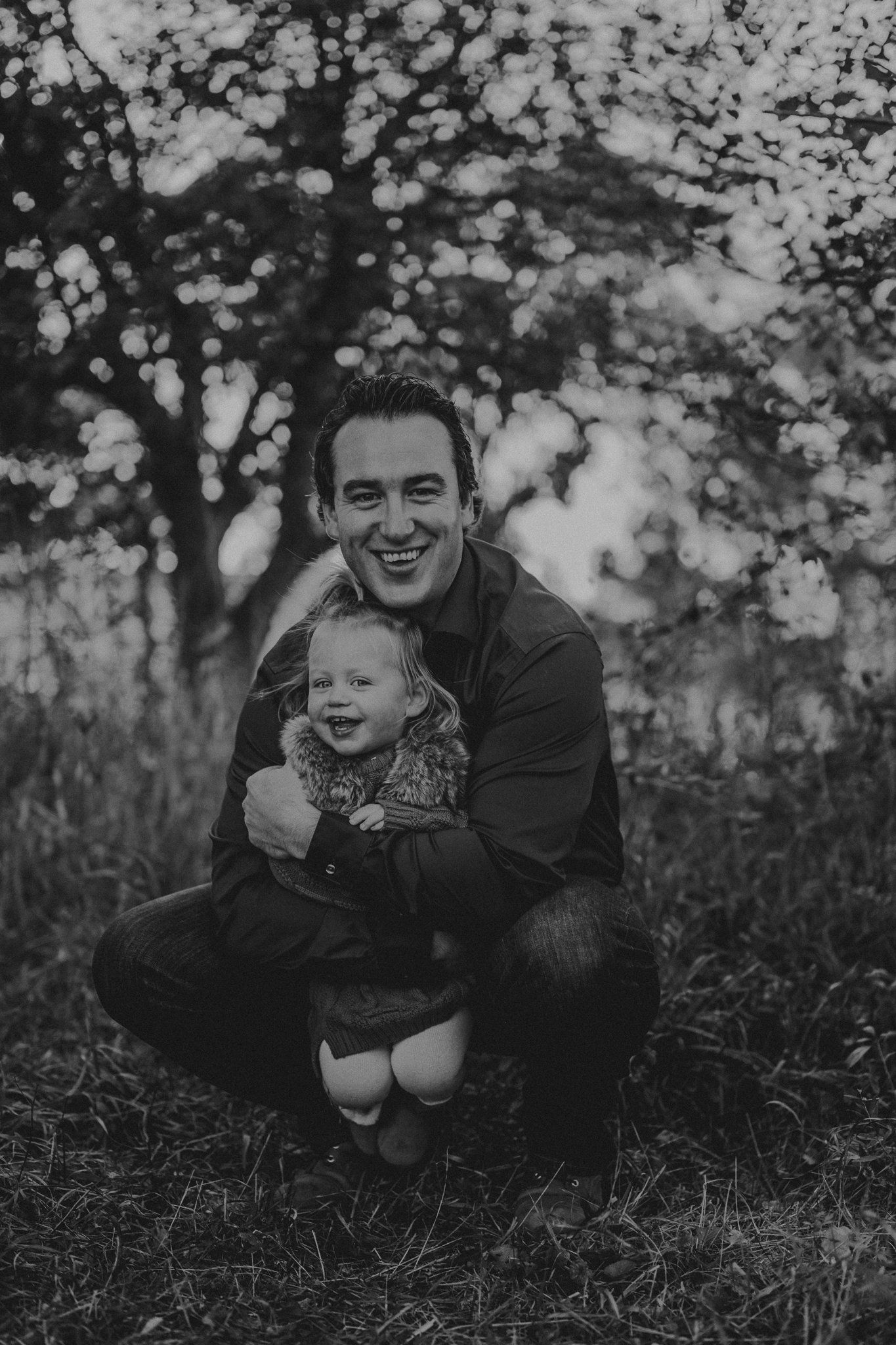 Black and white portrait of father and child sharing a happy moment outdoors among trees.