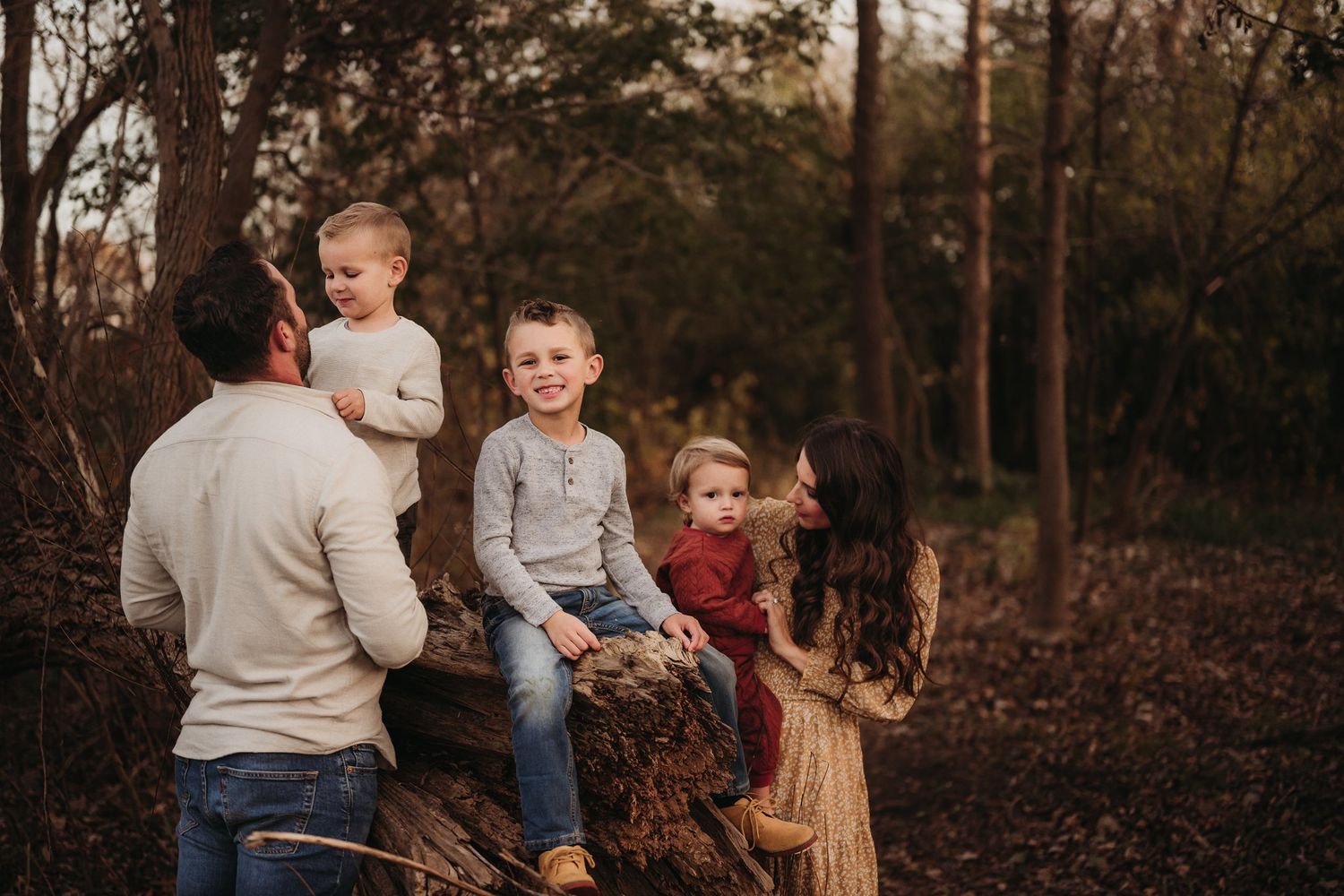 Natural light family portrait in a wooded setting with everyone positioned around a rustic tree stump.
