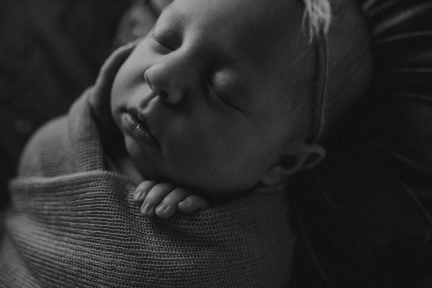 Close-up black and white image of sleeping newborn with hands tucked under chin.