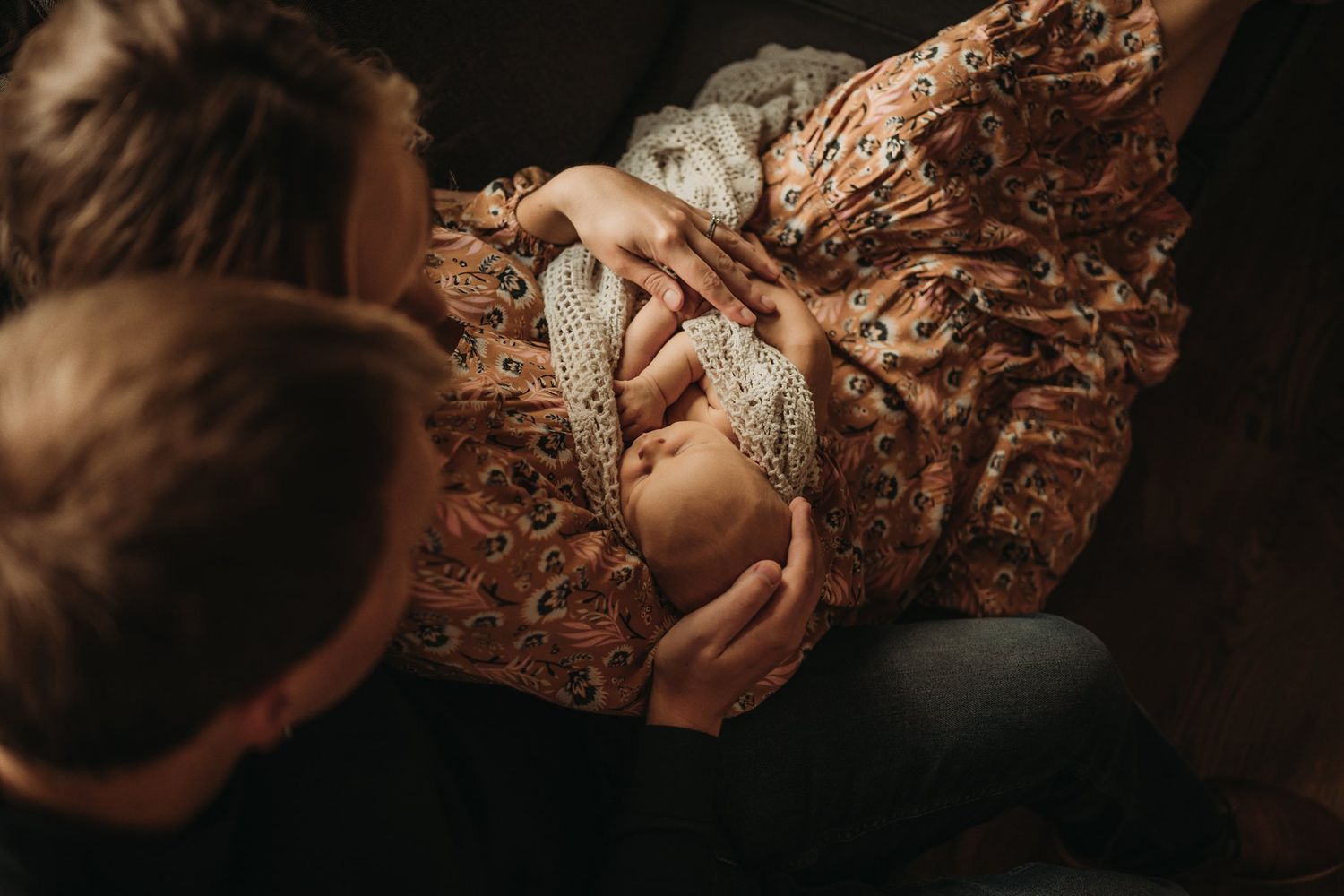 Intimate close-up shot of parents with newborn on brown couch.
