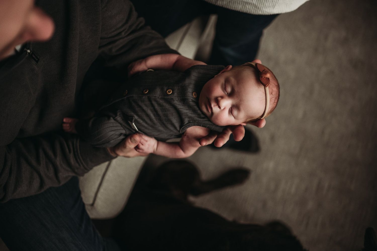 Overhead view of a baby lying on a dark cushioned surface in dim lighting.
