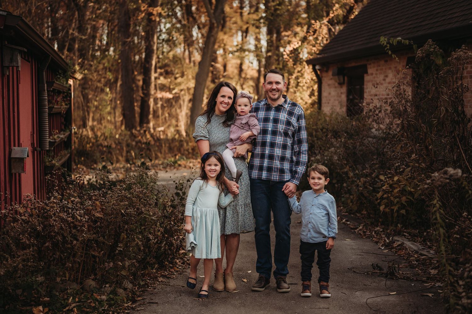 A family poses together on an autumn path with rustic buildings in the background.