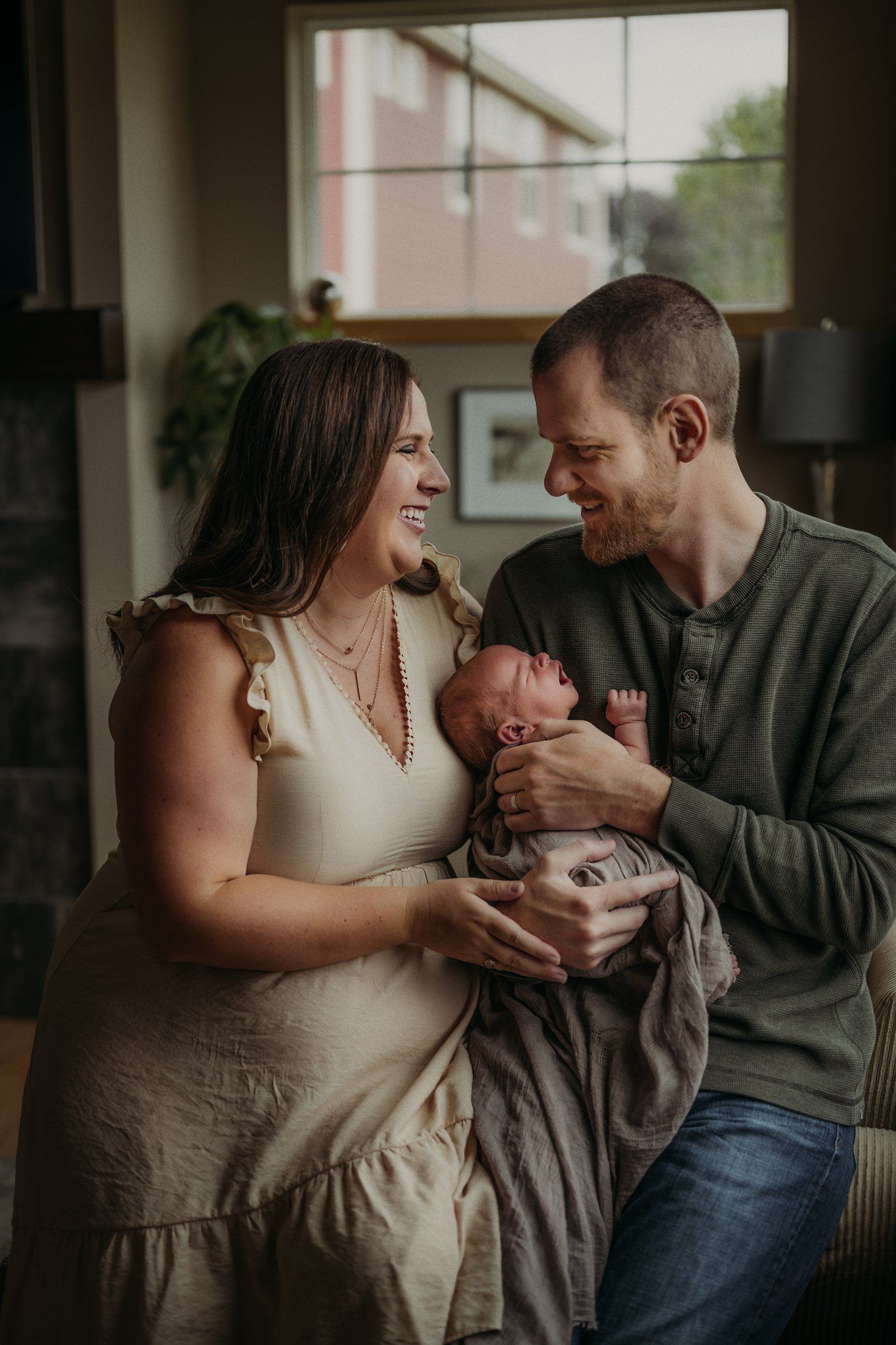 Family sharing tender moment with newborn baby in living room setting.
