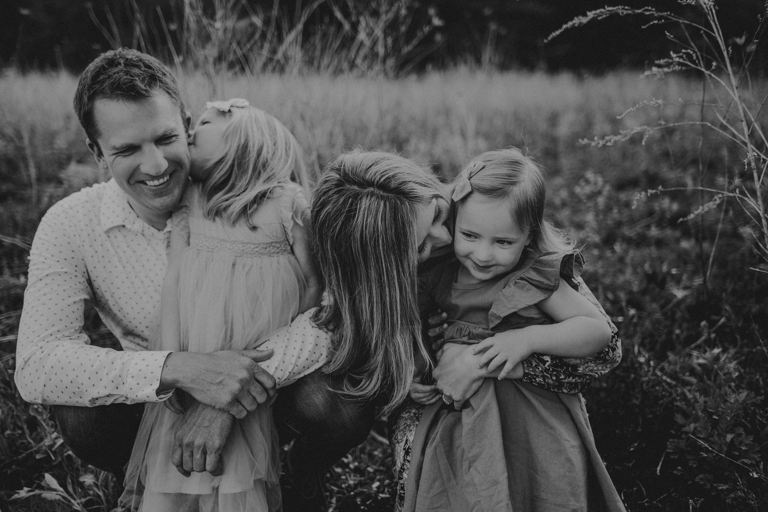 Black and white portrait of family sharing playful moment in field.