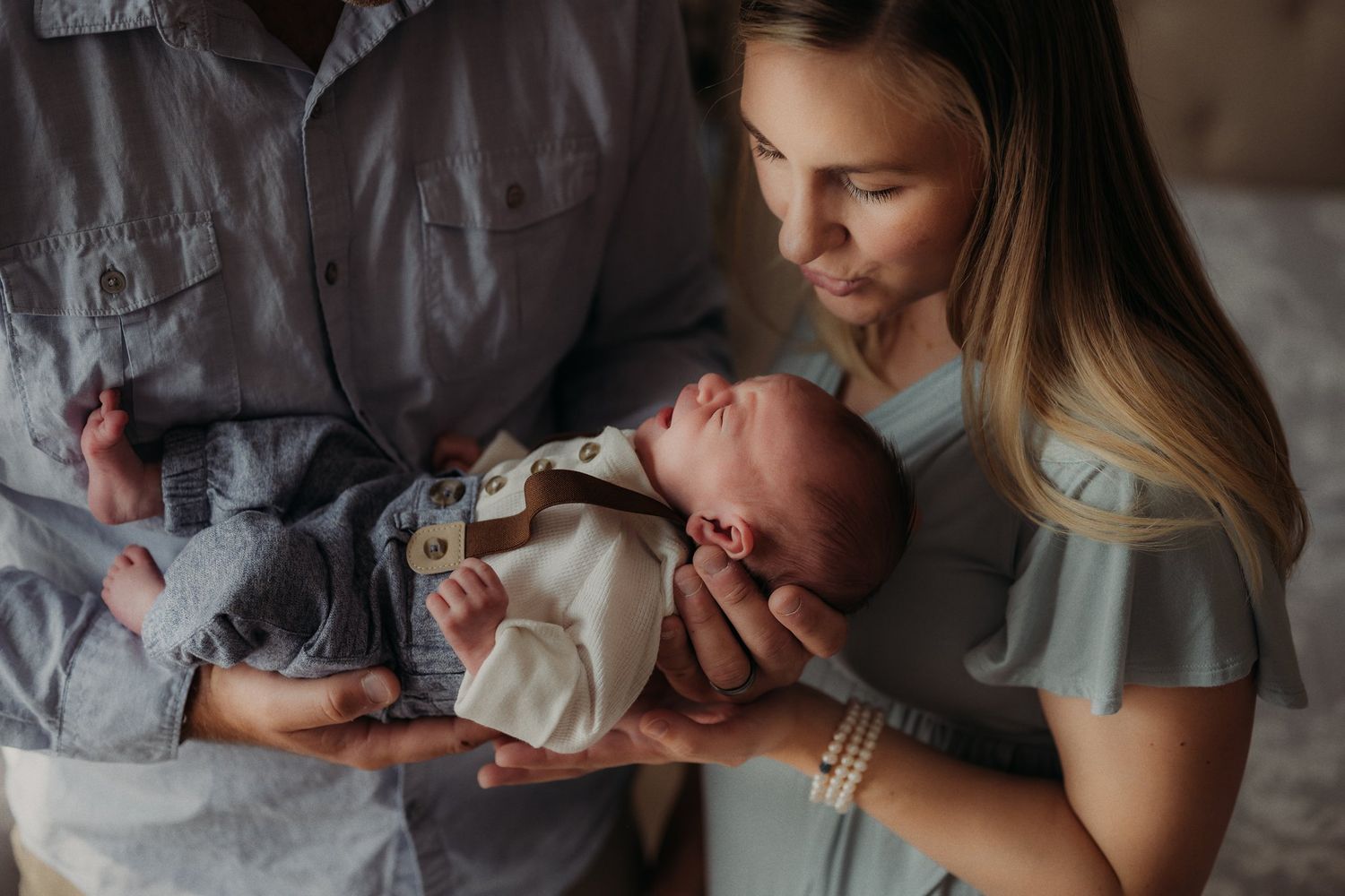 Parents lovingly hold their newborn baby in natural window light.