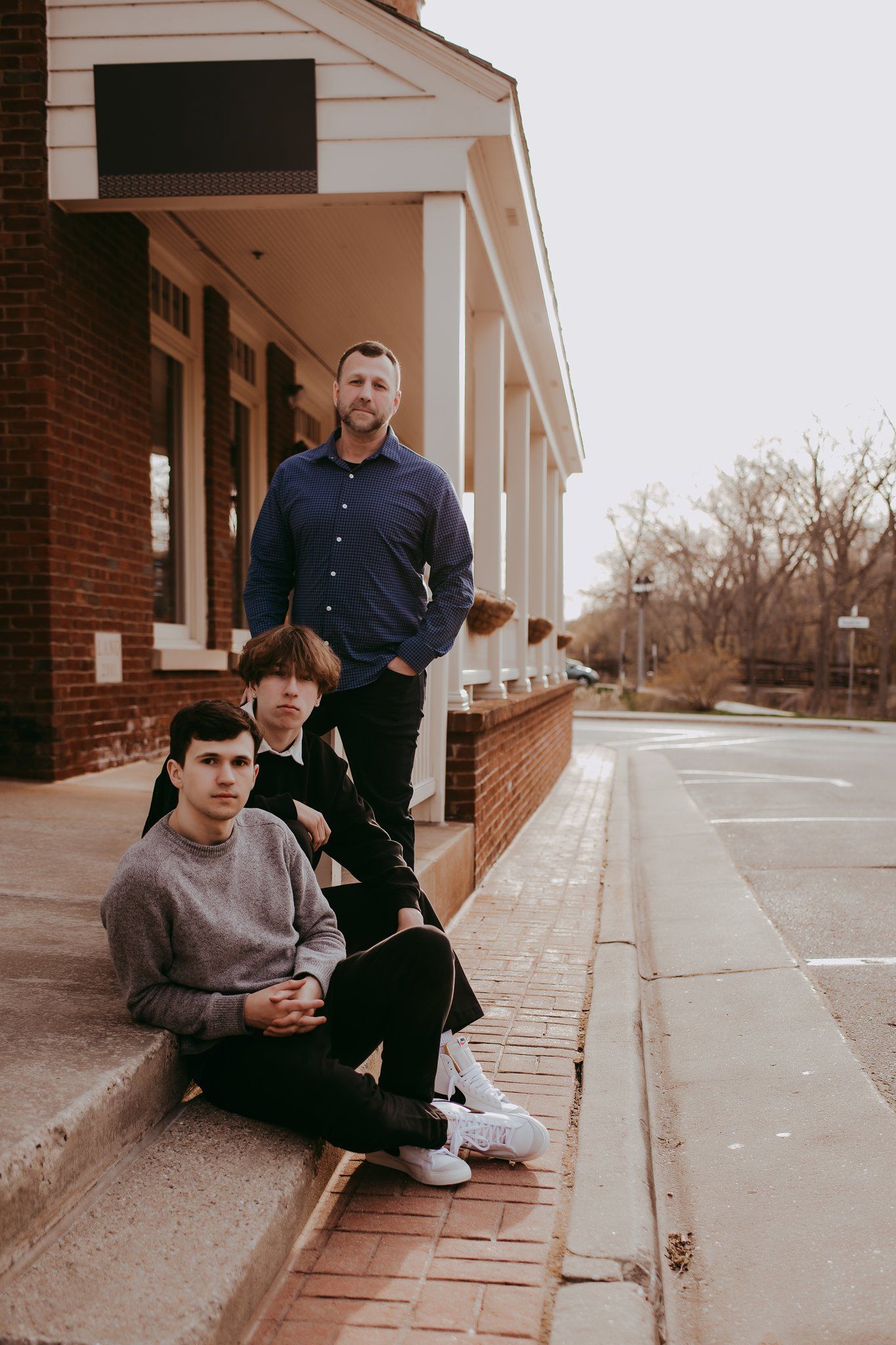 Three people pose casually outside a brick building with white columns.