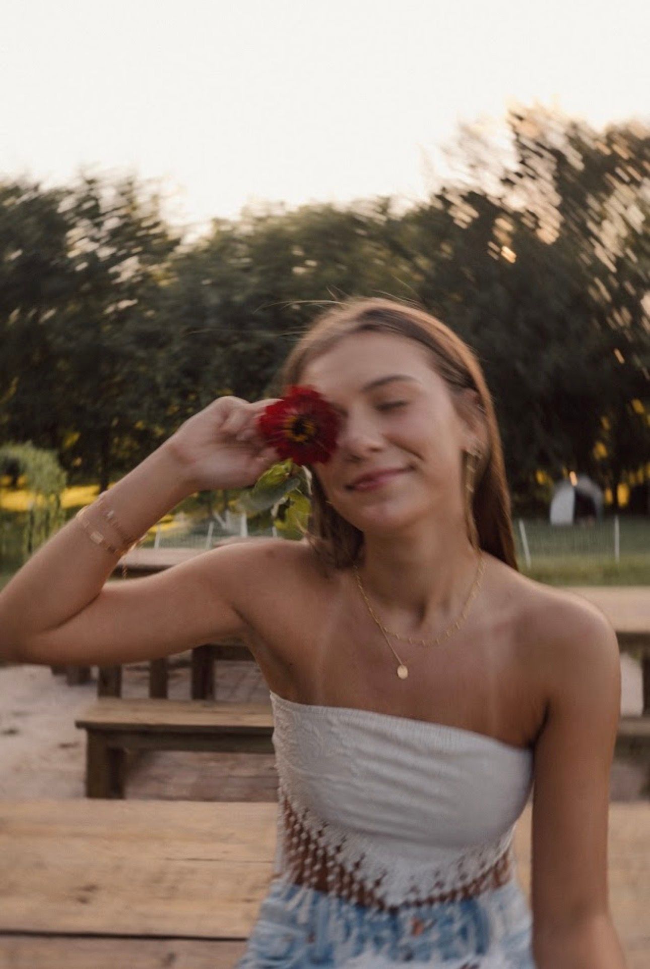A summer portrait of someone holding a red flower while wearing a white top at sunset.