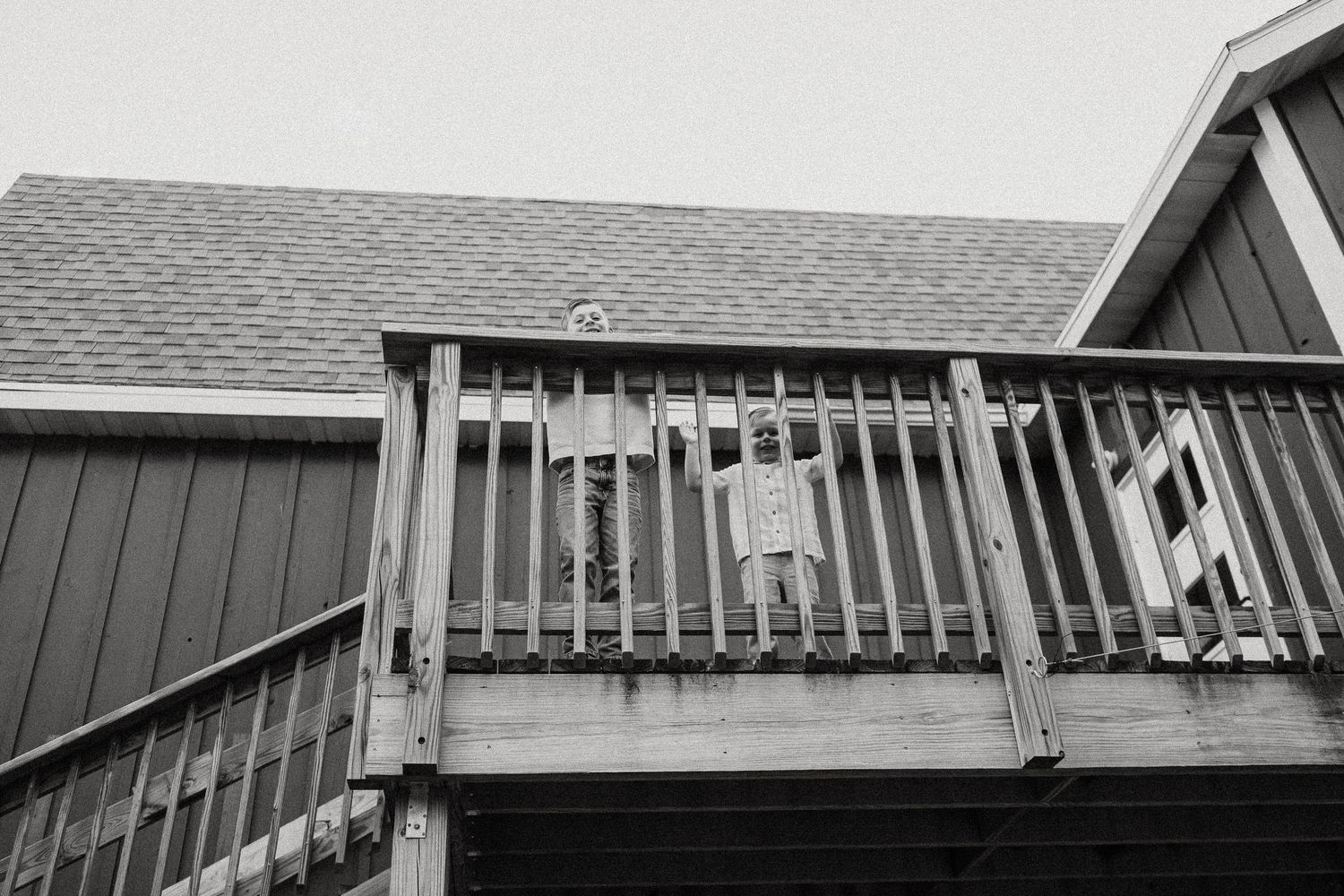 Black and white photo of a young child standing on a wooden deck balcony of a barn-style building.