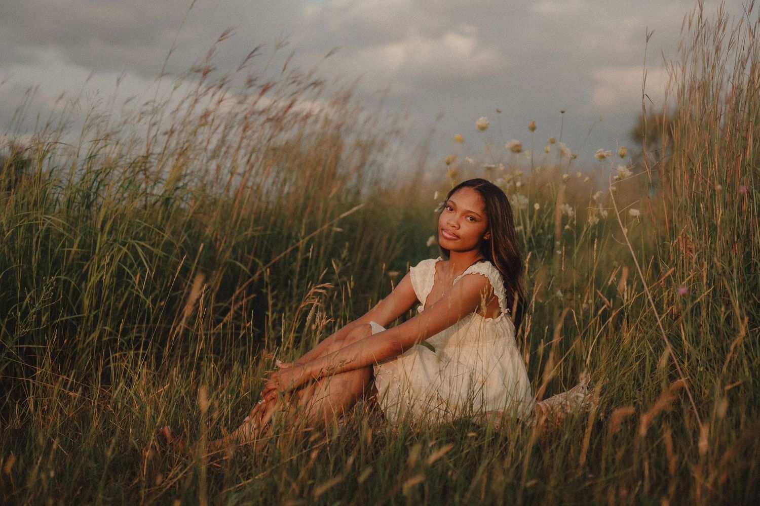 Young woman in white dress sitting peacefully in a golden field of tall grass.