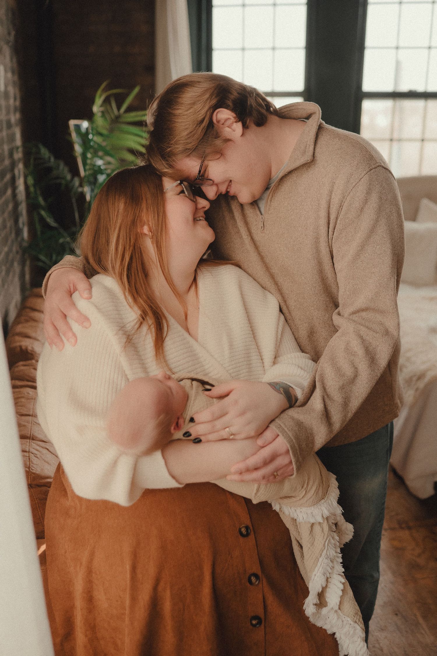 Couple sharing a tender forehead-to-forehead moment, embracing in a cozy bedroom setting.
