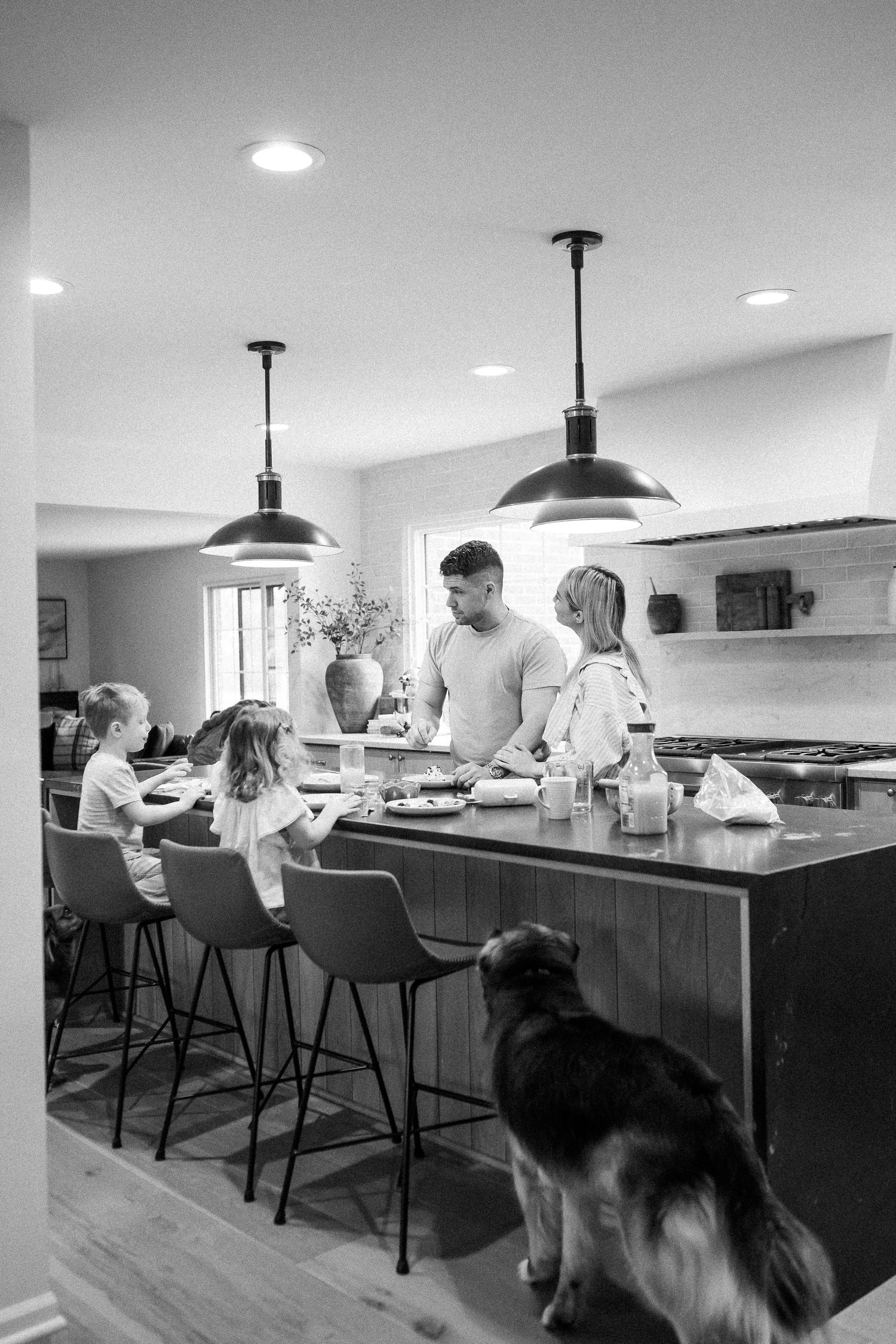Black and white photo of a family at a kitchen island with a dog in the foreground.