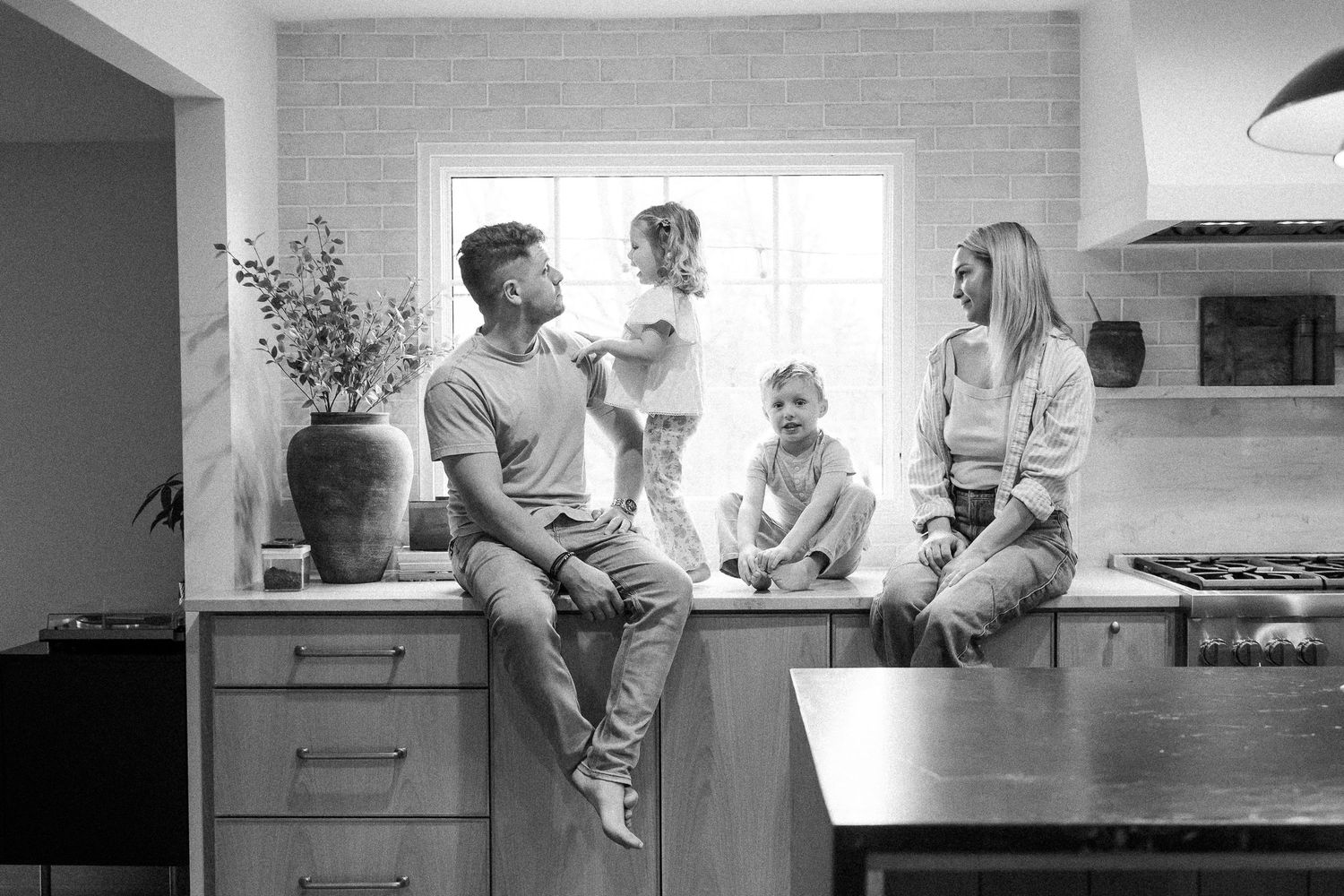 Black and white family portrait of parents and two young children sitting together on a kitchen counter.