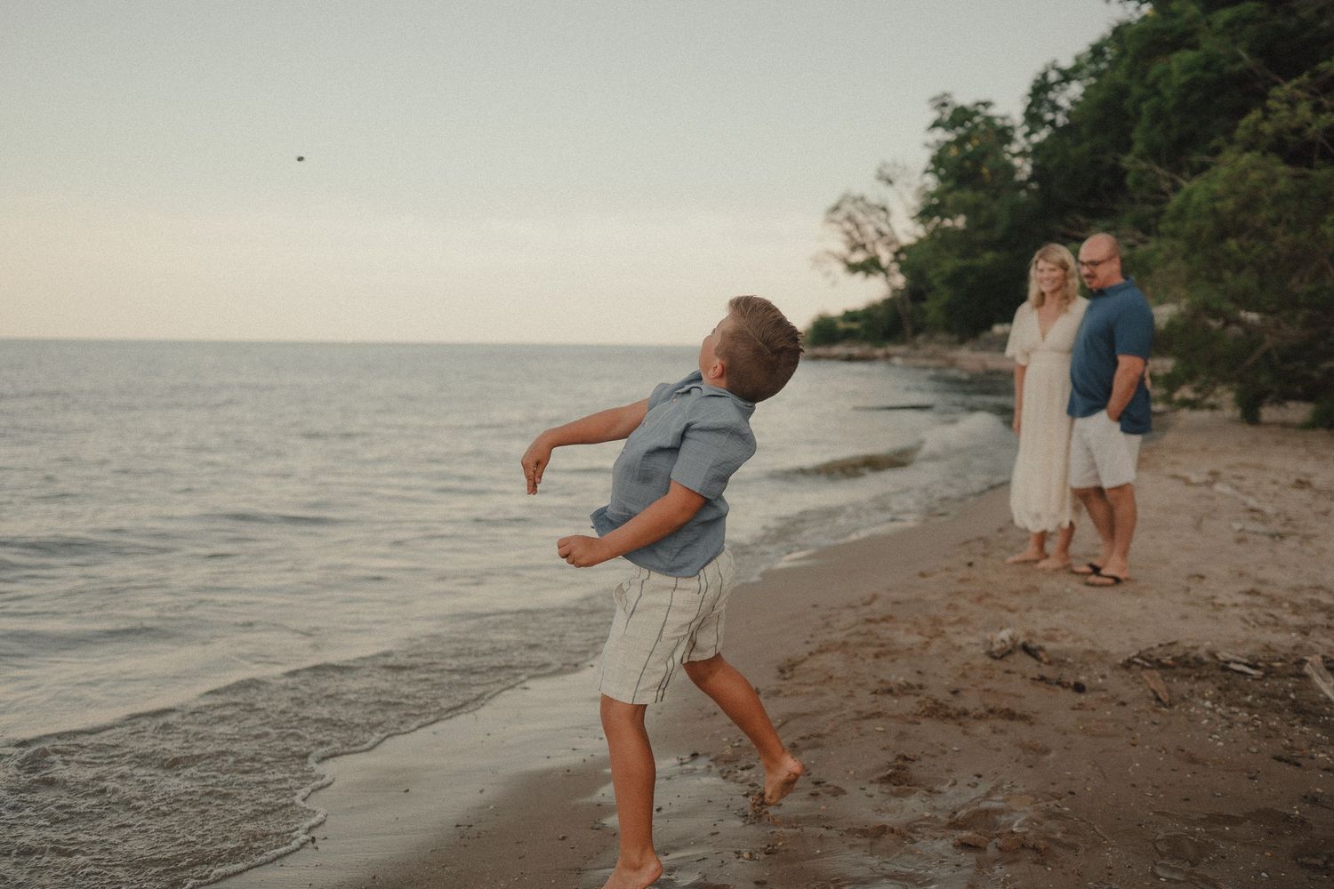 Family enjoying sunset on beach, boy throwing rocks into ocean while parents watch.