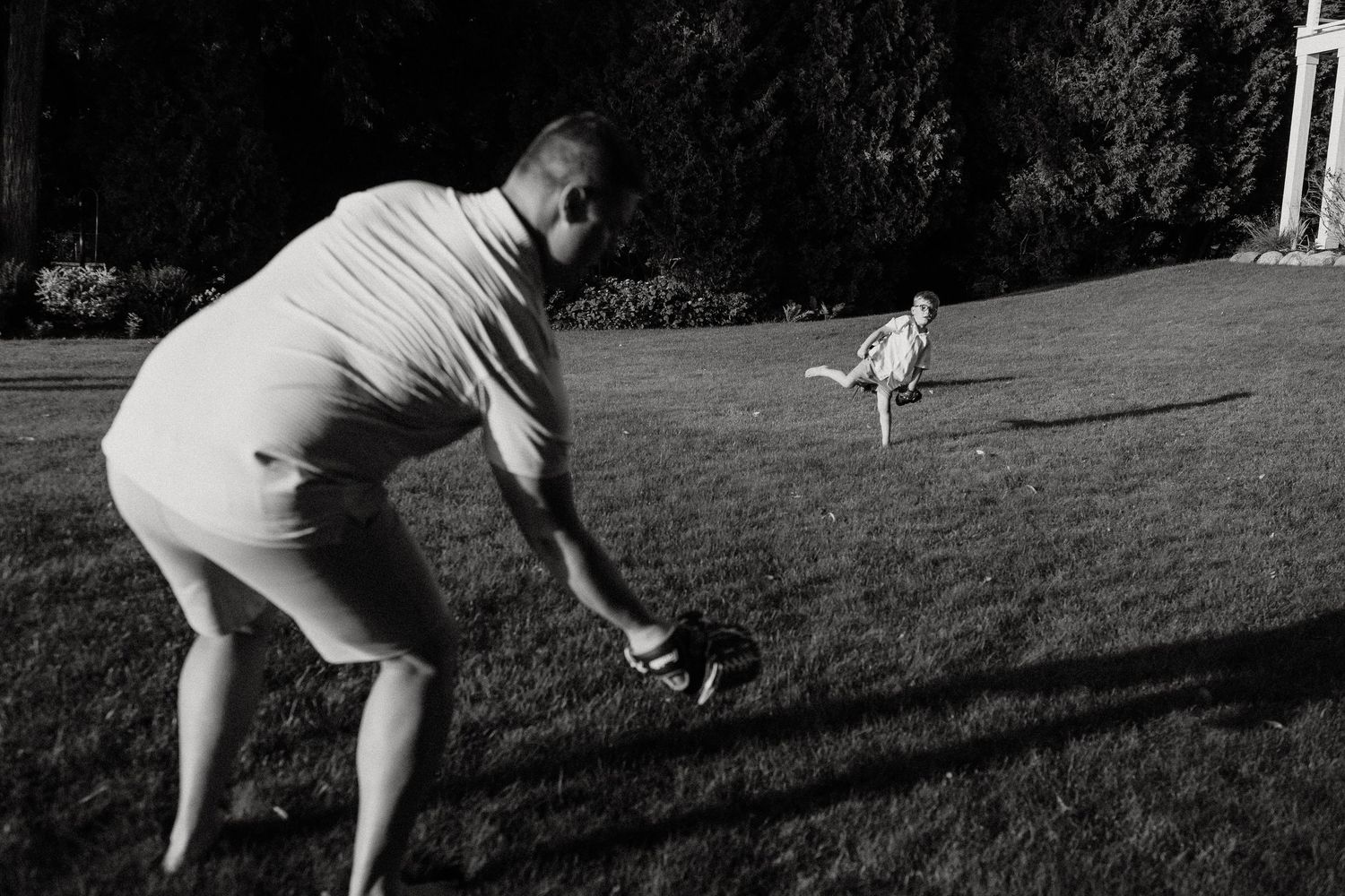 Black and white photo of a man bending down as a child runs across a sunny green lawn outdoors.