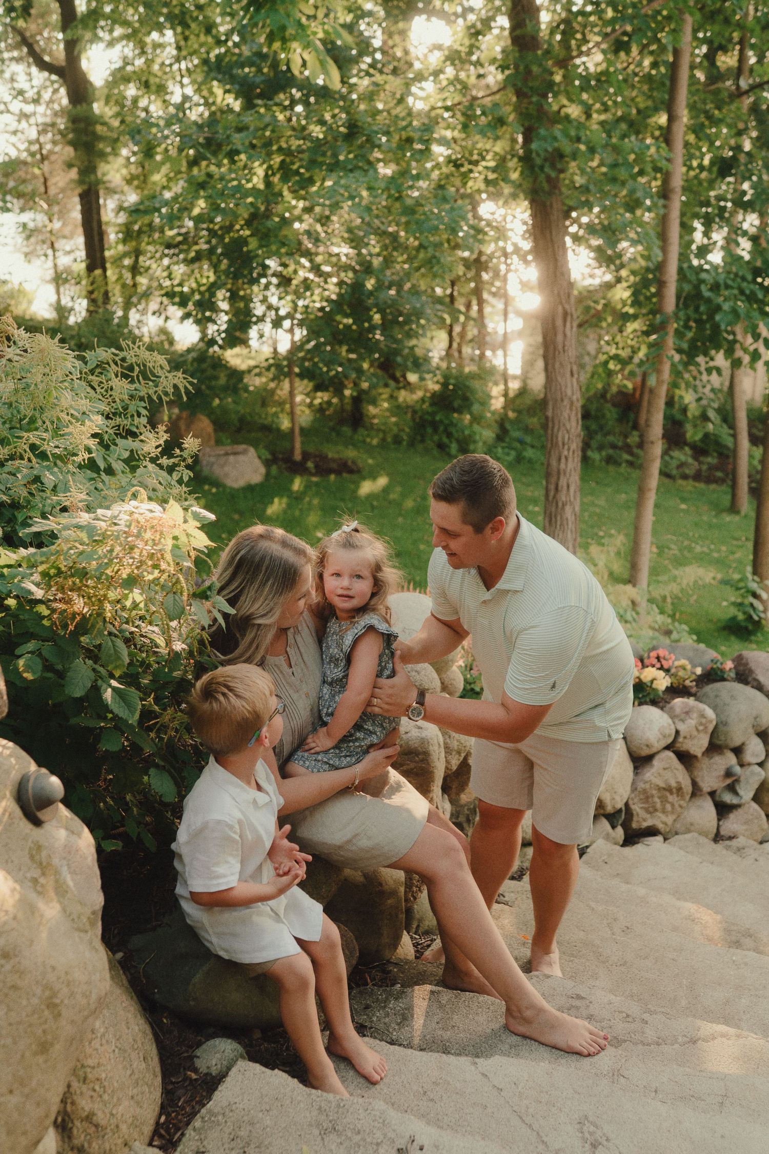 Family of four enjoying golden hour in a lush garden, sitting on rocks surrounded by greenery.