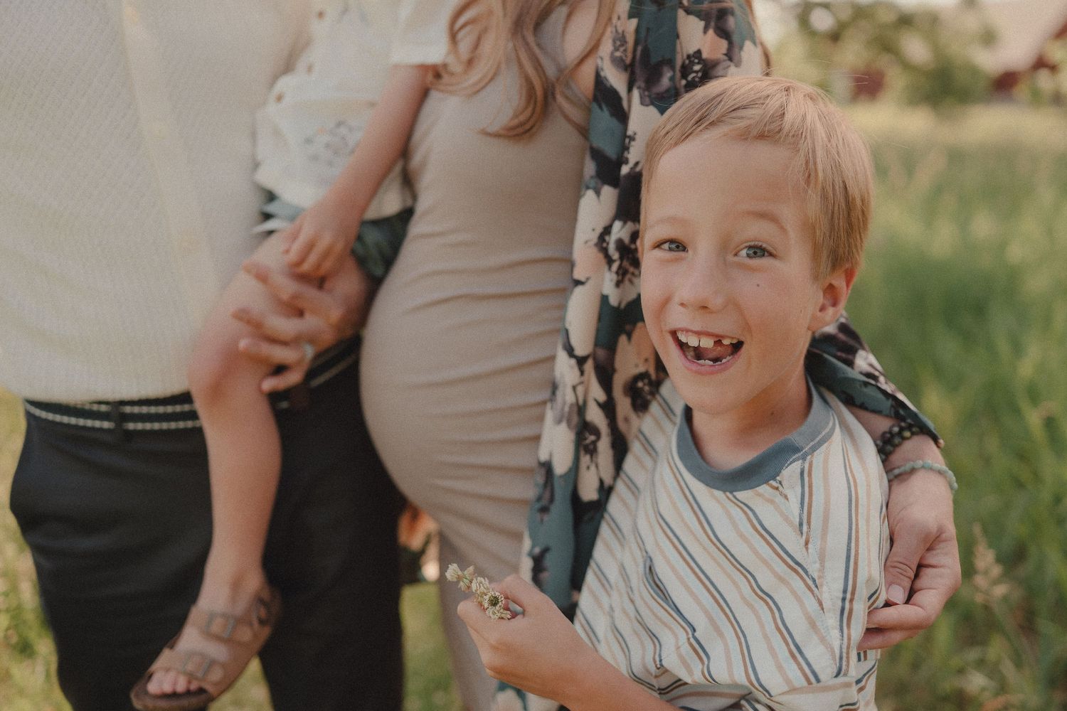 A smiling boy stands in front of his pregnant mother and father during an outdoor maternity photo session.